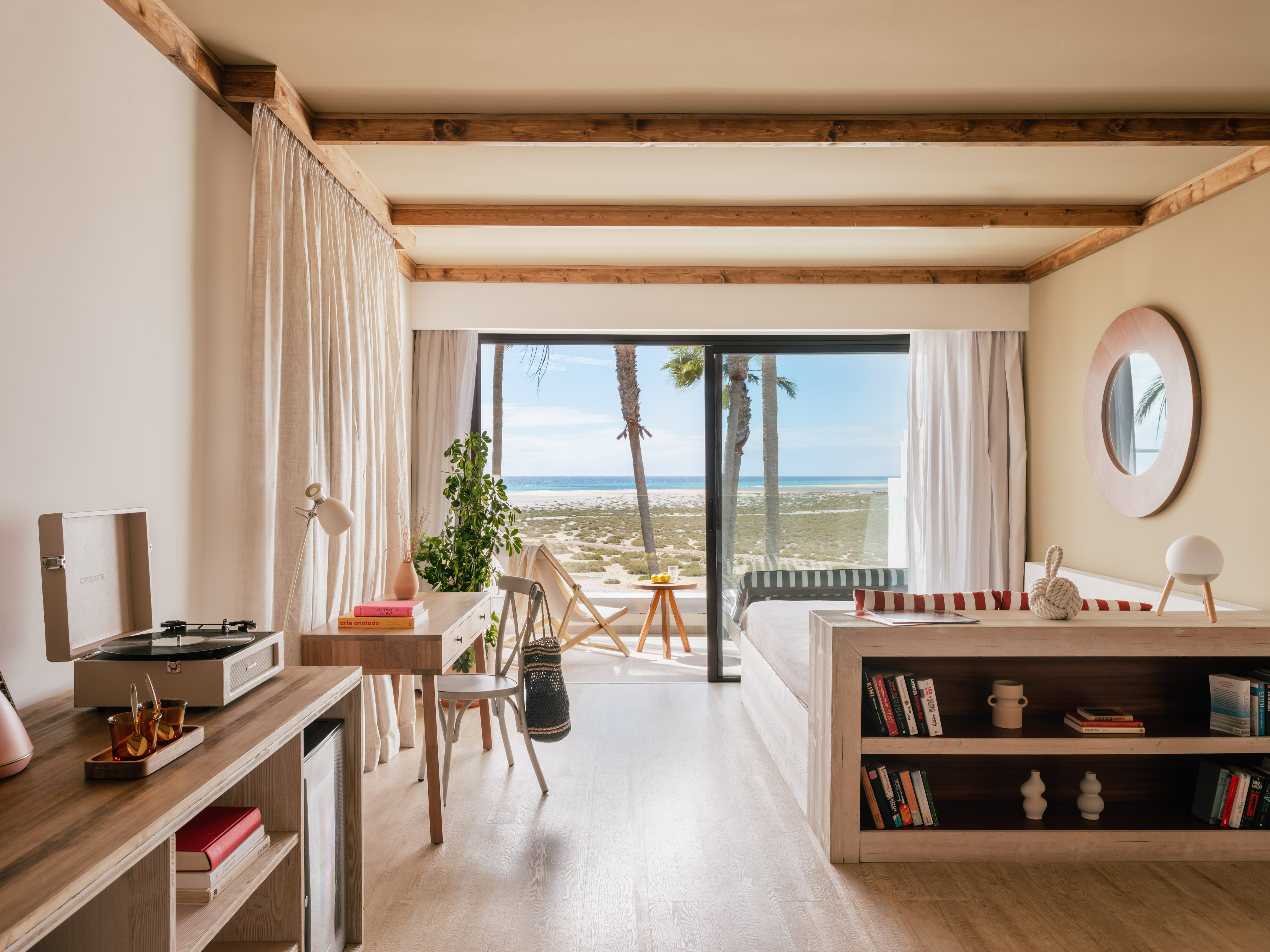 Modern beachfront room with ocean view, palm trees, and light wood interior.