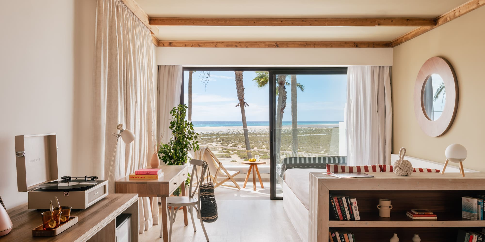 Modern beachfront room with ocean view, palm trees, and light wood interior.