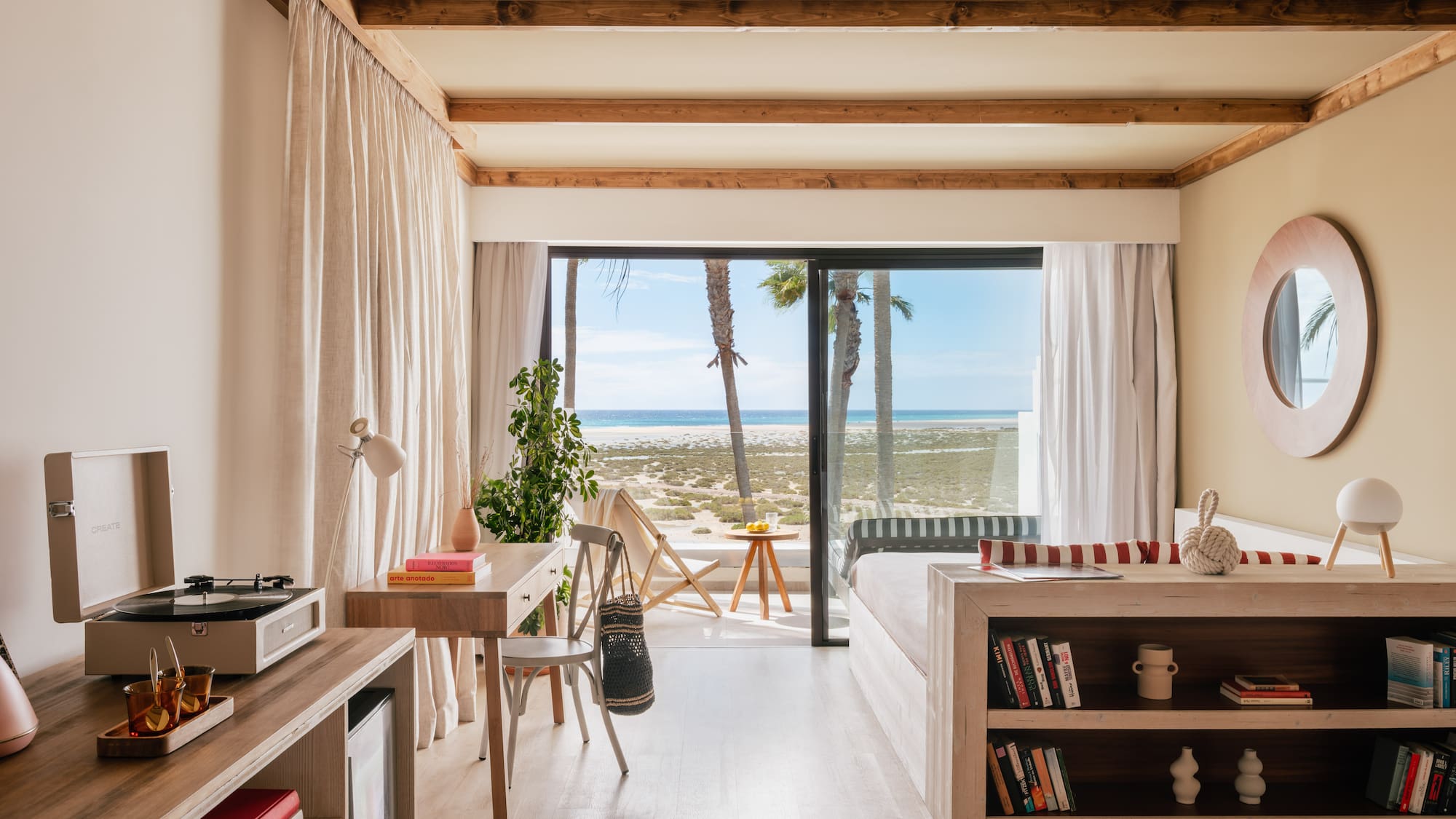 Modern beachfront room with ocean view, palm trees, and light wood interior.