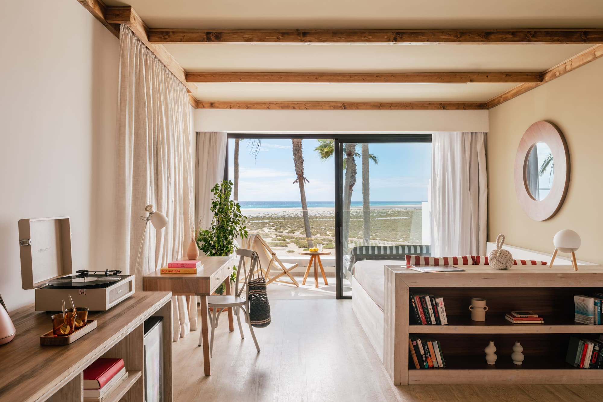 Modern beachfront room with ocean view, palm trees, and light wood interior.