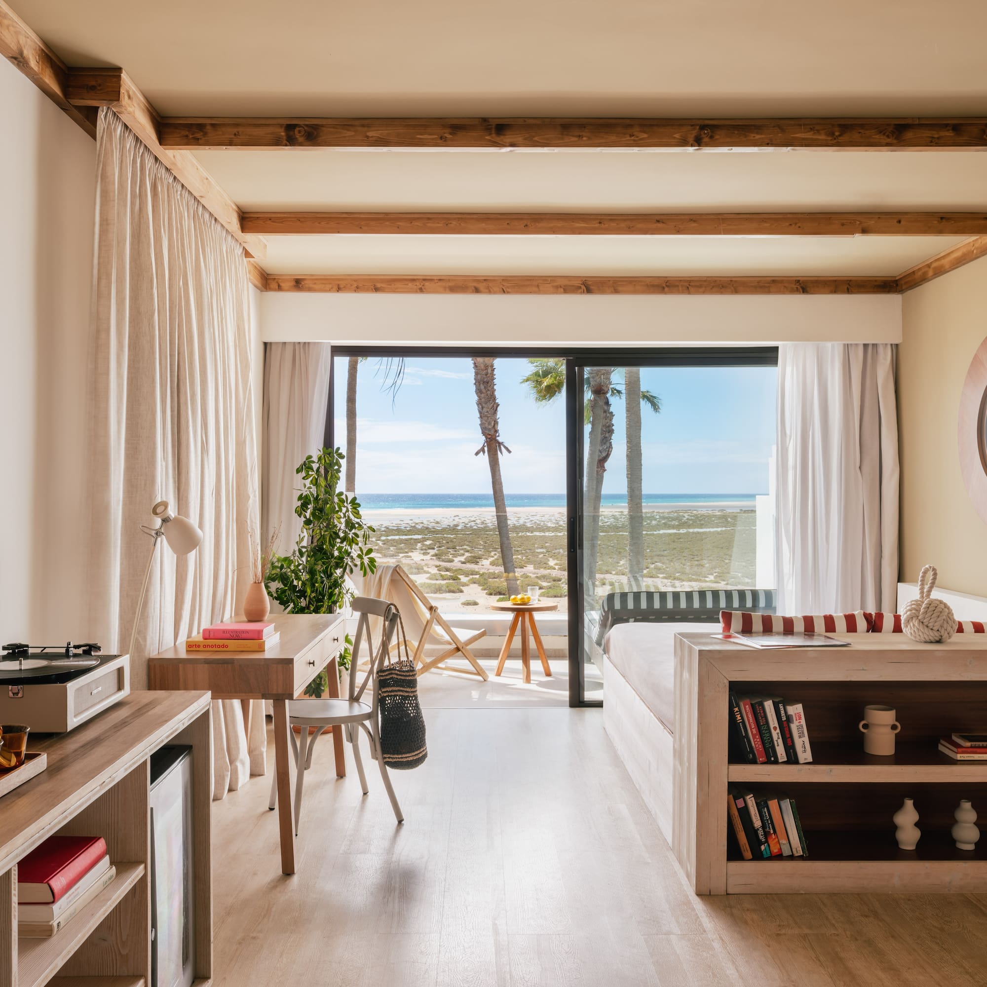 Modern beachfront room with ocean view, palm trees, and light wood interior.