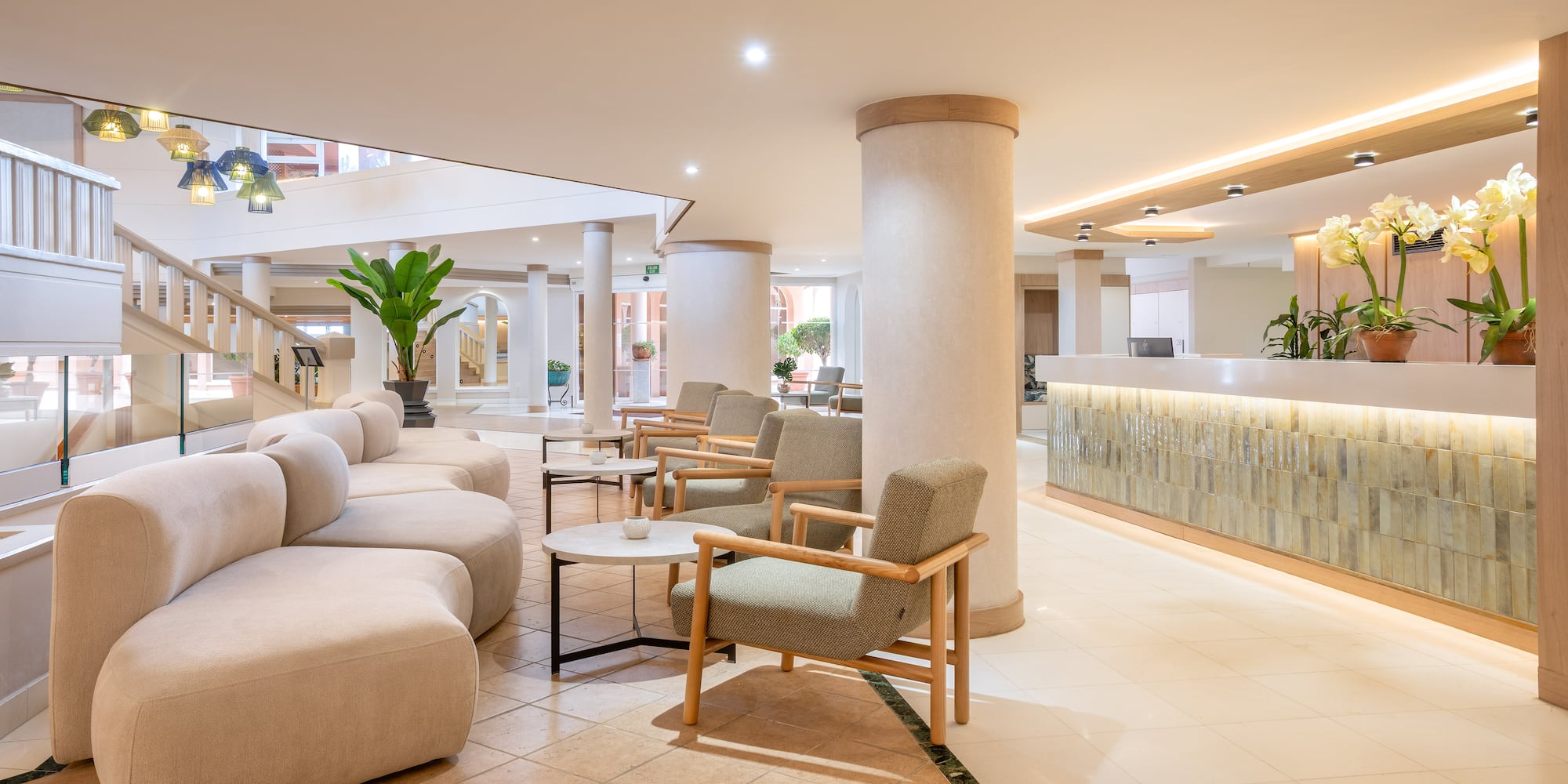 Modern hotel lobby with reception desk, curved sofa, and green plants.