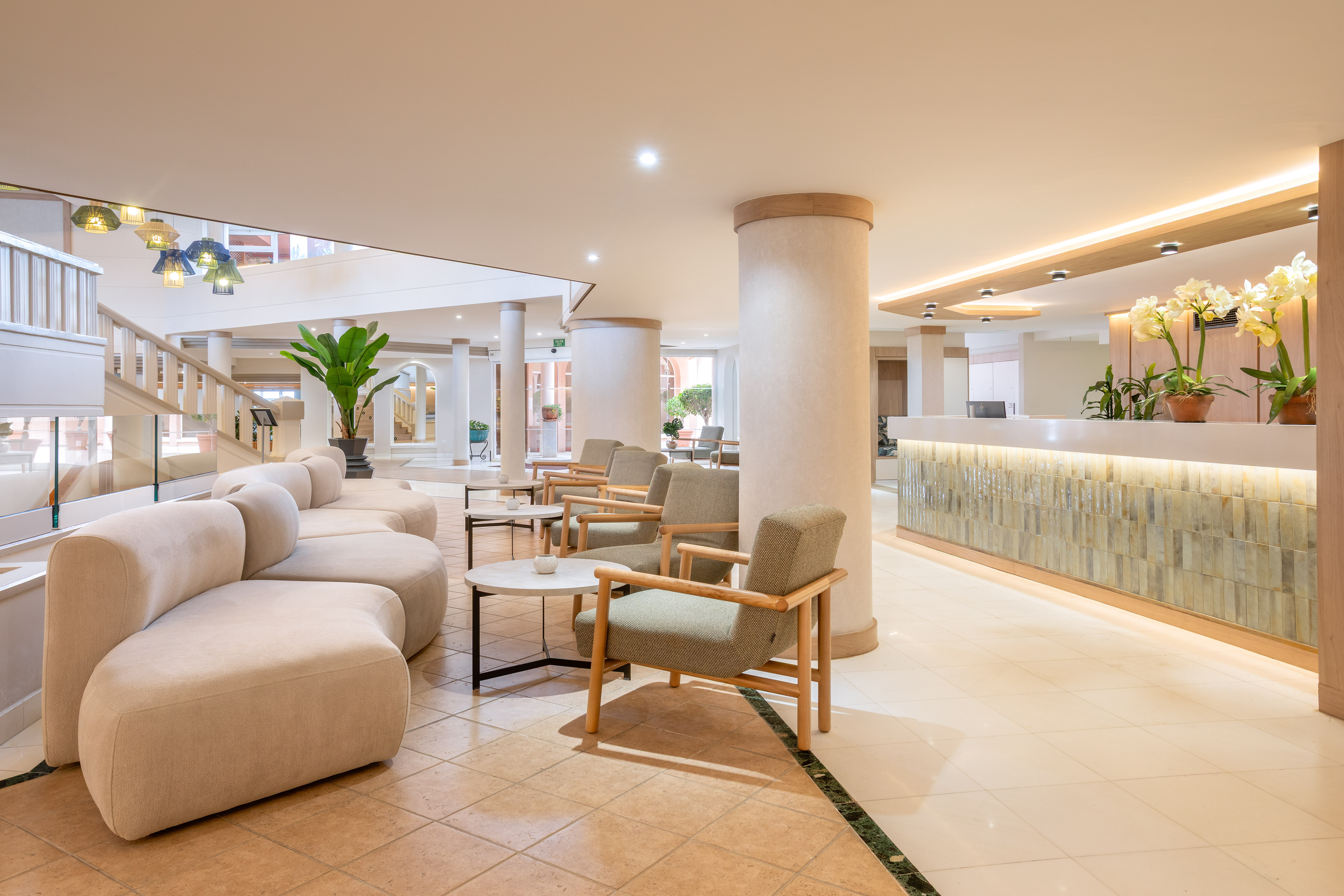 Modern hotel lobby with reception desk, curved sofa, and green plants.
