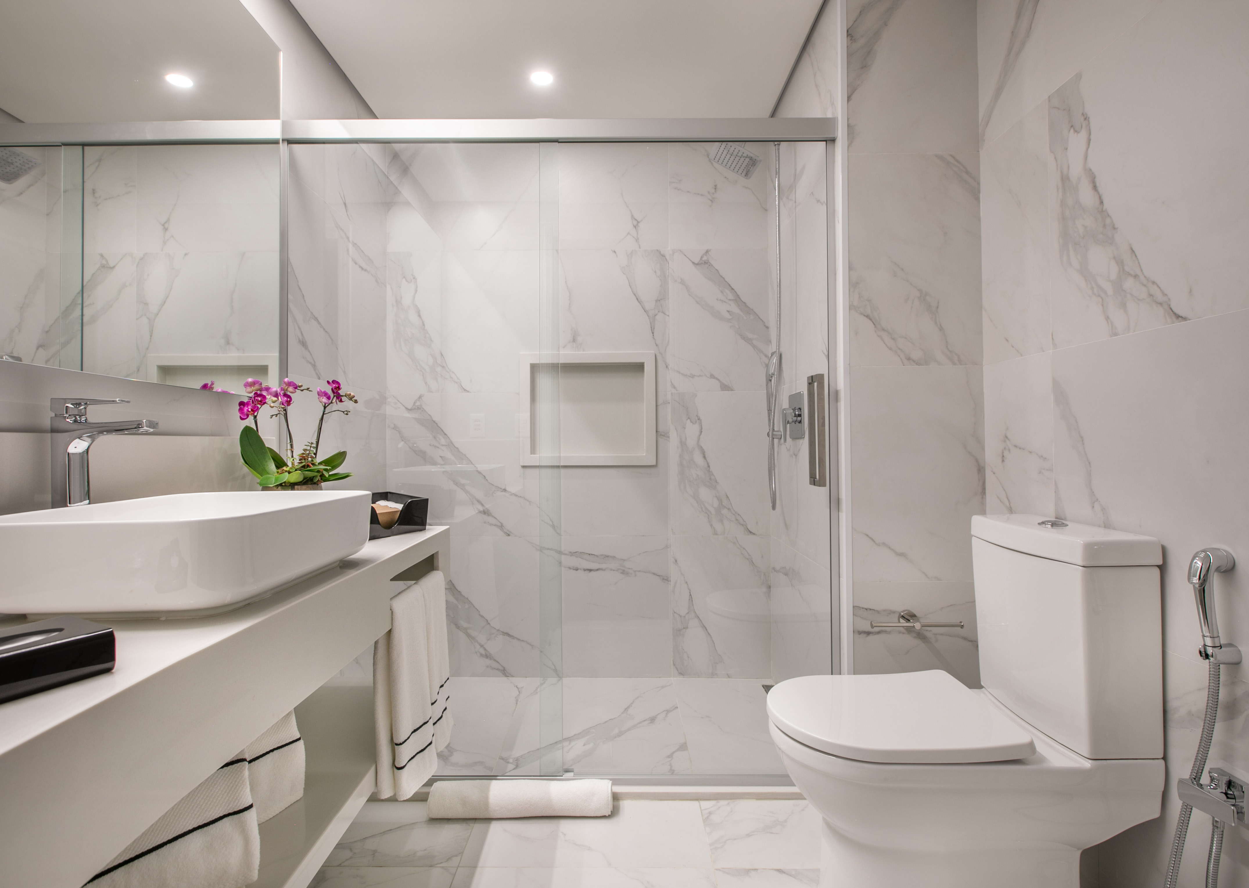 Modern white marble bathroom with glass shower, vessel sink vanity, and toilet.