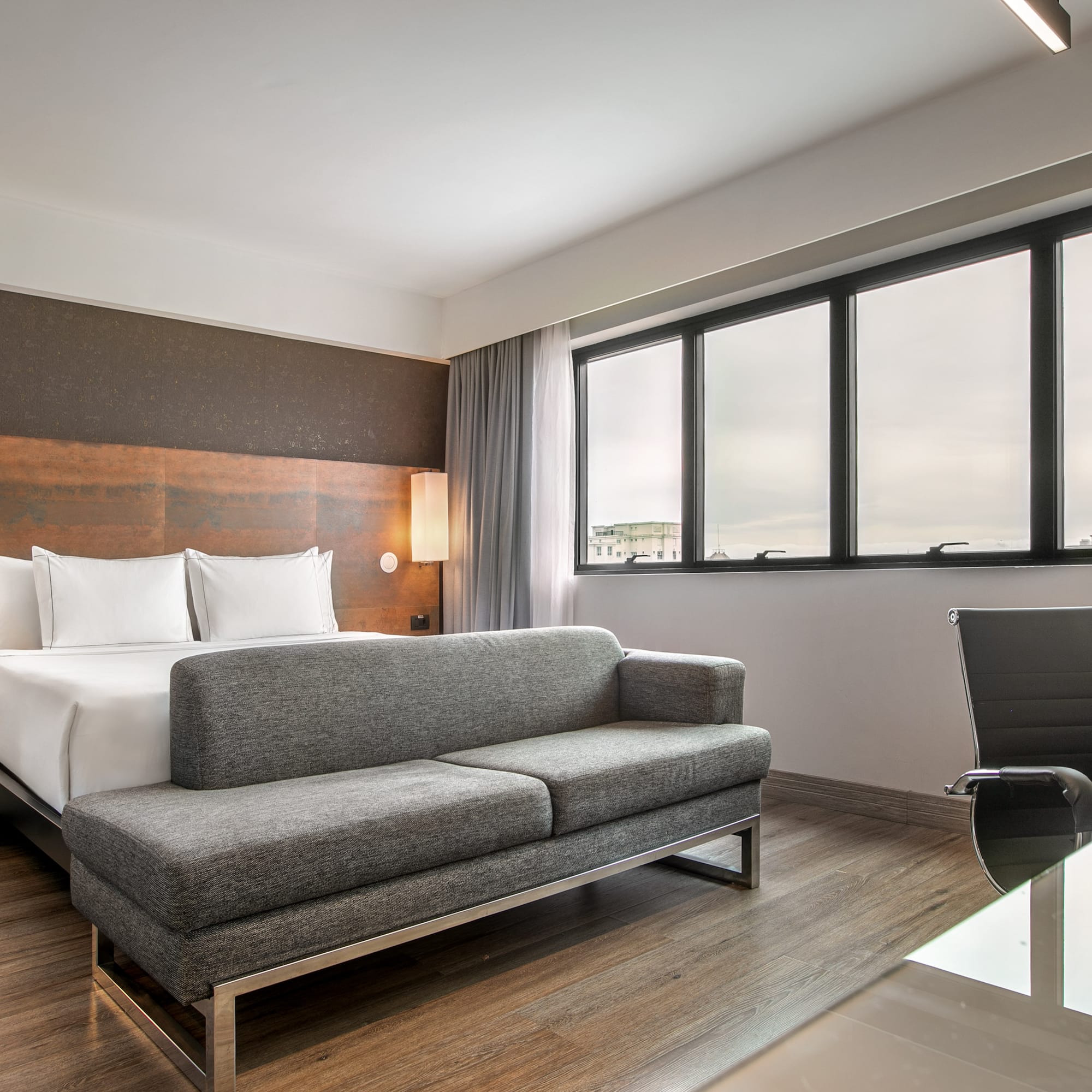 Quarto de hotel moderno com cama de casal, sofá cinza e escrivaninha. - Grand Premium - Meliá Ibirapuera, São Paulo