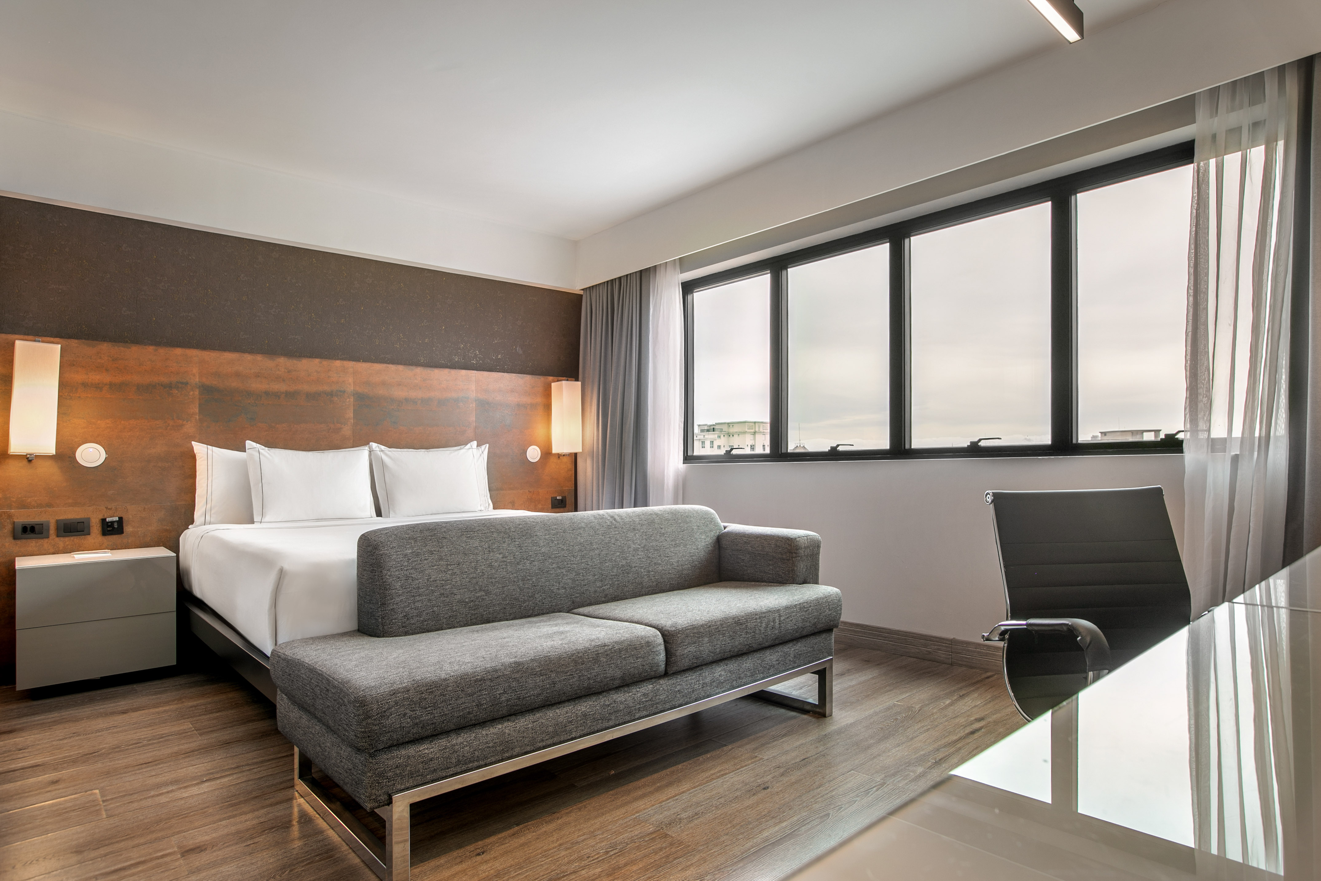 Quarto de hotel moderno com cama de casal, sofá cinza e escrivaninha. - Grand Premium - Meliá Ibirapuera, São Paulo