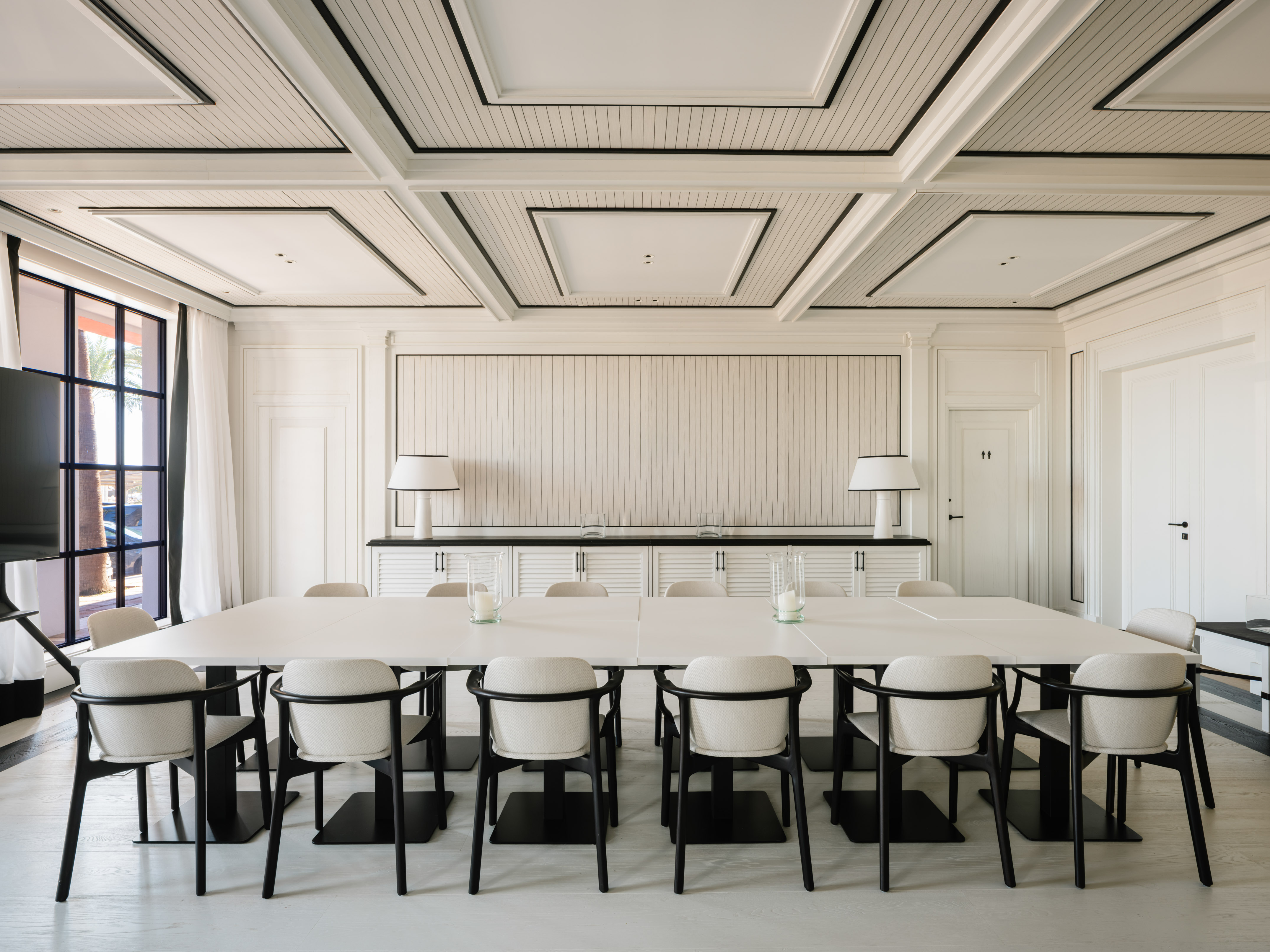 Modern white meeting room with large table, black chairs, coffered ceiling.