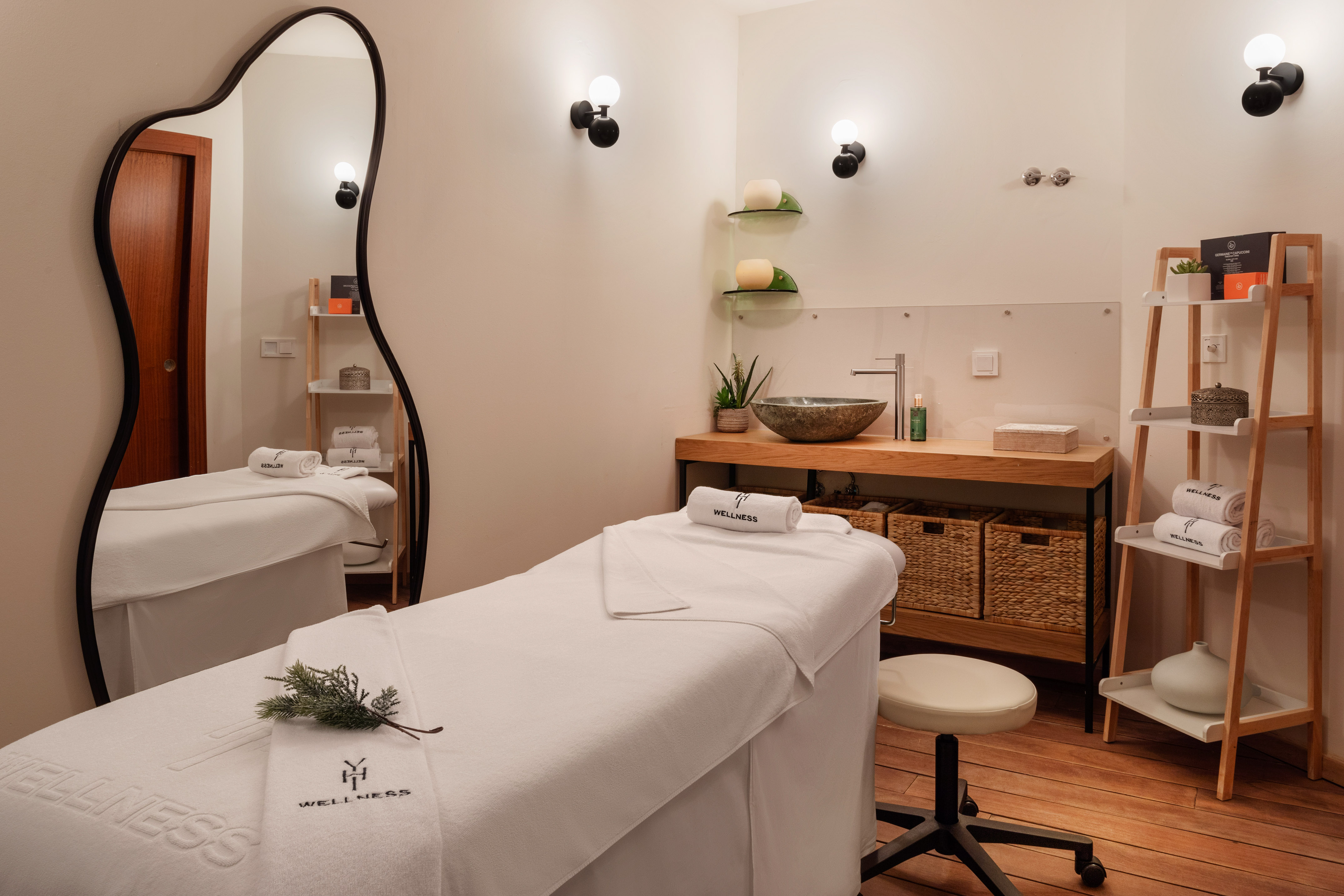 Modern wellness spa treatment room with massage bed, stone sink, and elegant mirror.
