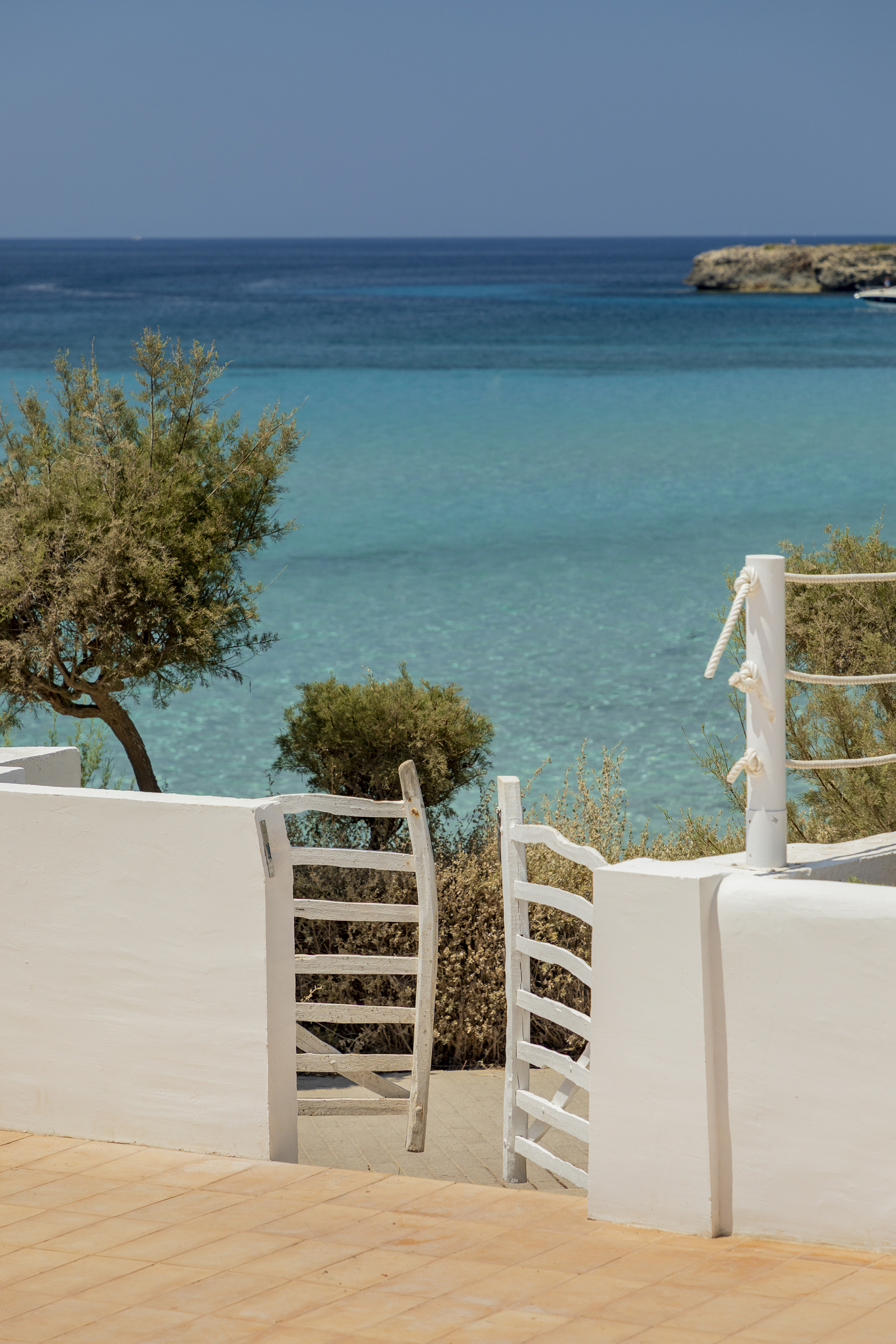 a white wall with a white gate and trees and a blue body of water