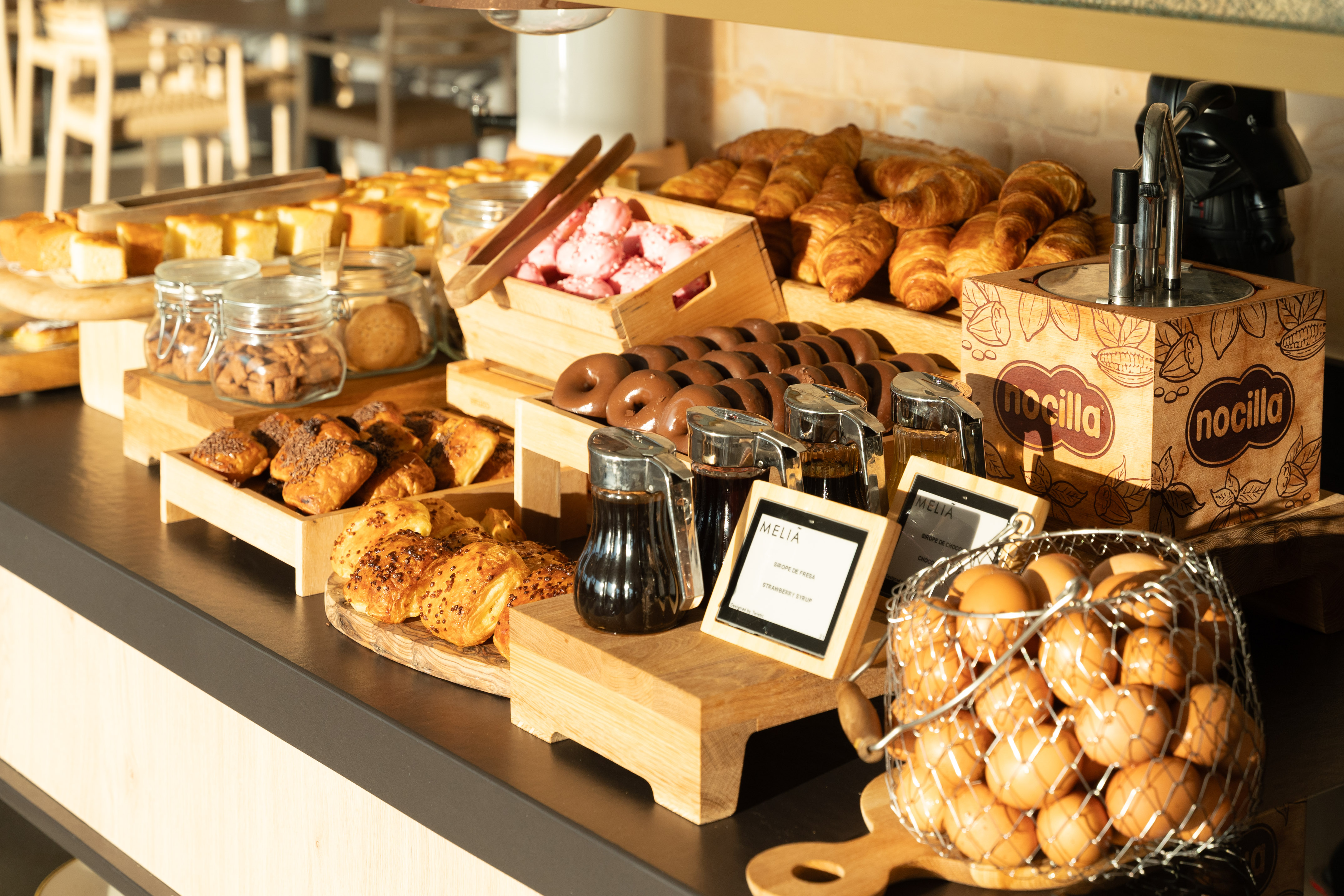 Hotel breakfast buffet with croissants, chocolate donuts, cakes, eggs, and Nocilla.