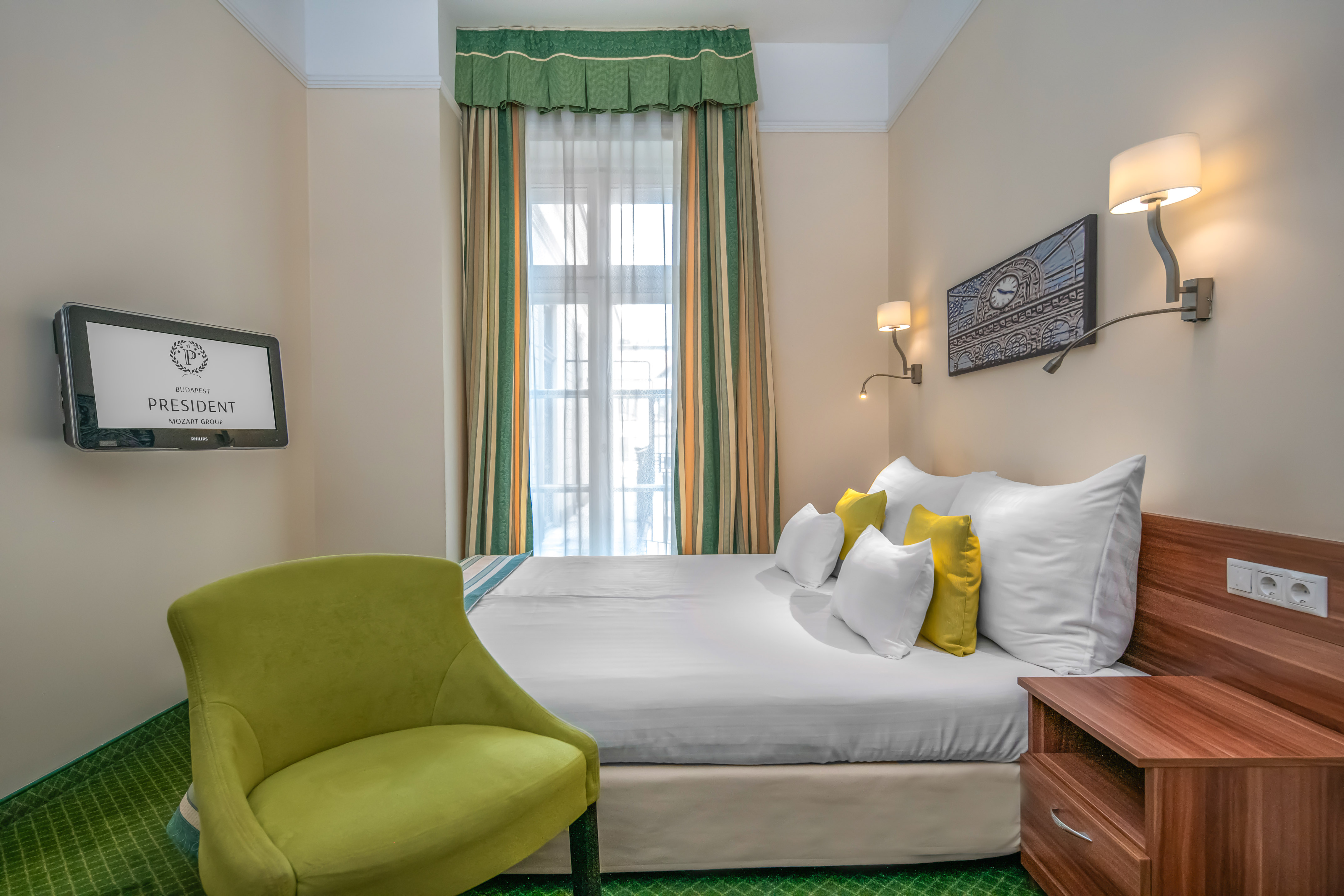 Budapest PRESIDENT hotel room with bed, green armchair, TV, and patterned curtains. - Standard Classic - Hotel President Budapest Affiliated by Meliá, Budapest