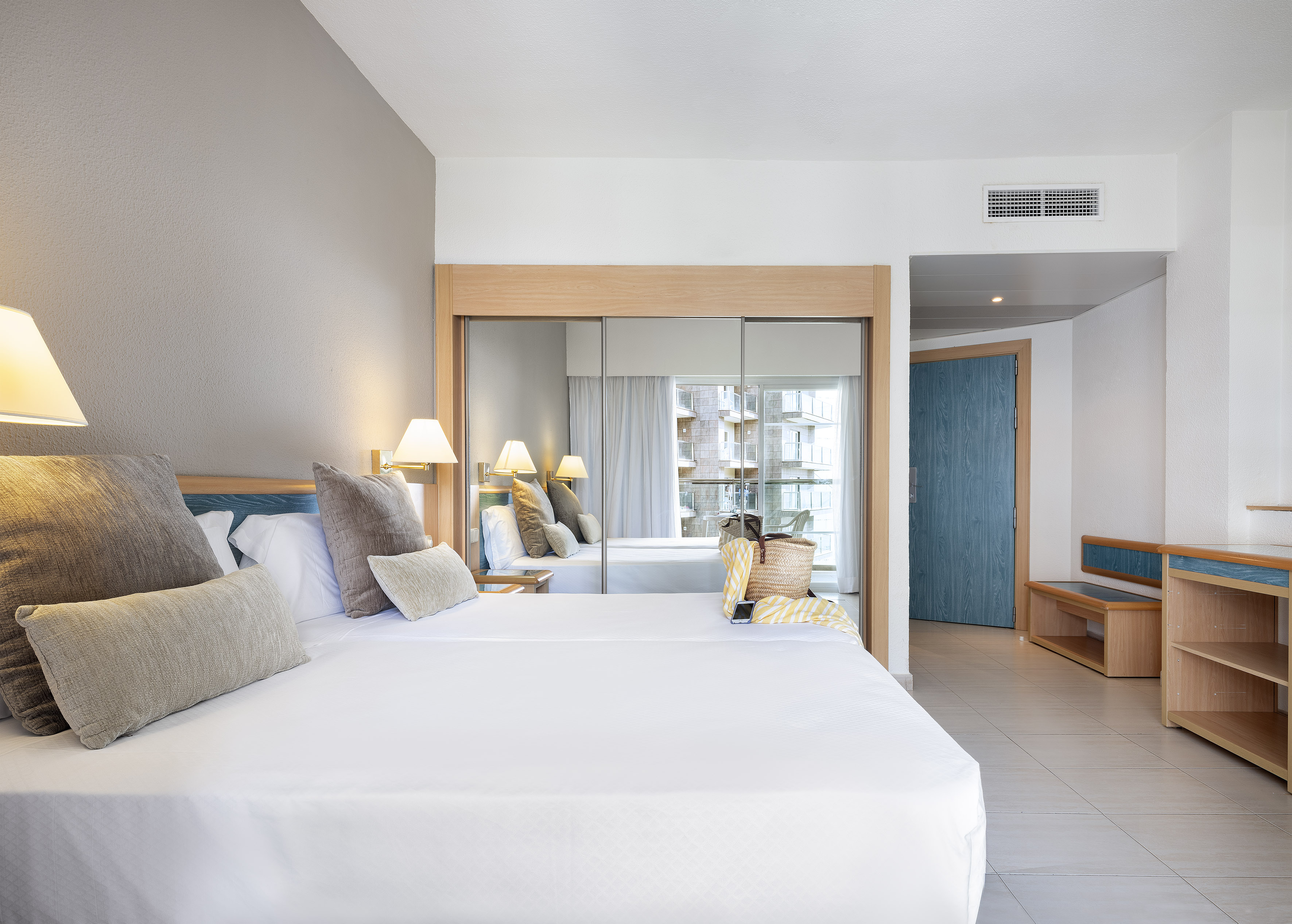 Modern hotel room with large bed, mirrored closet, and balcony view.