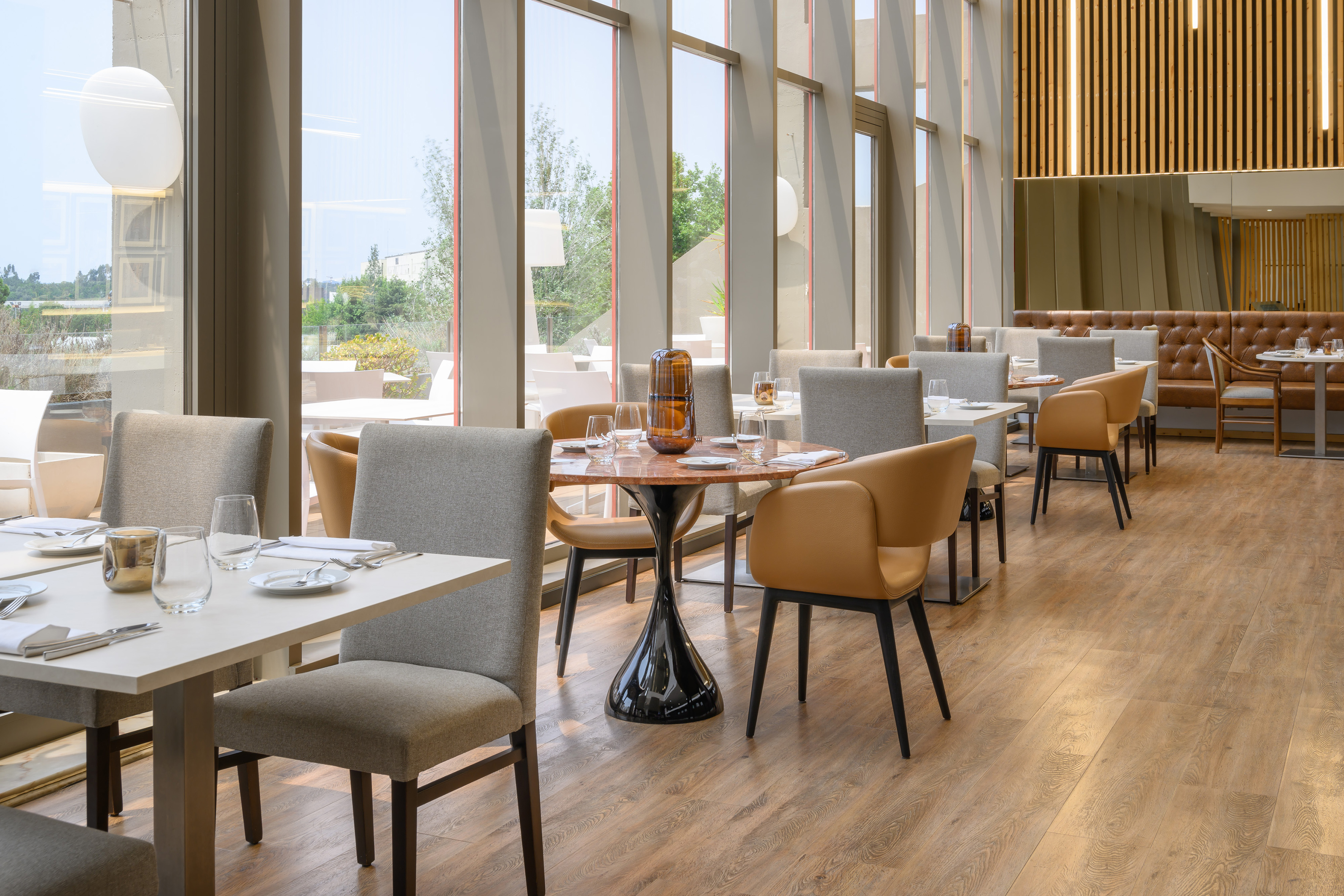 Bright modern restaurant dining room with large windows, wood floors, set tables.