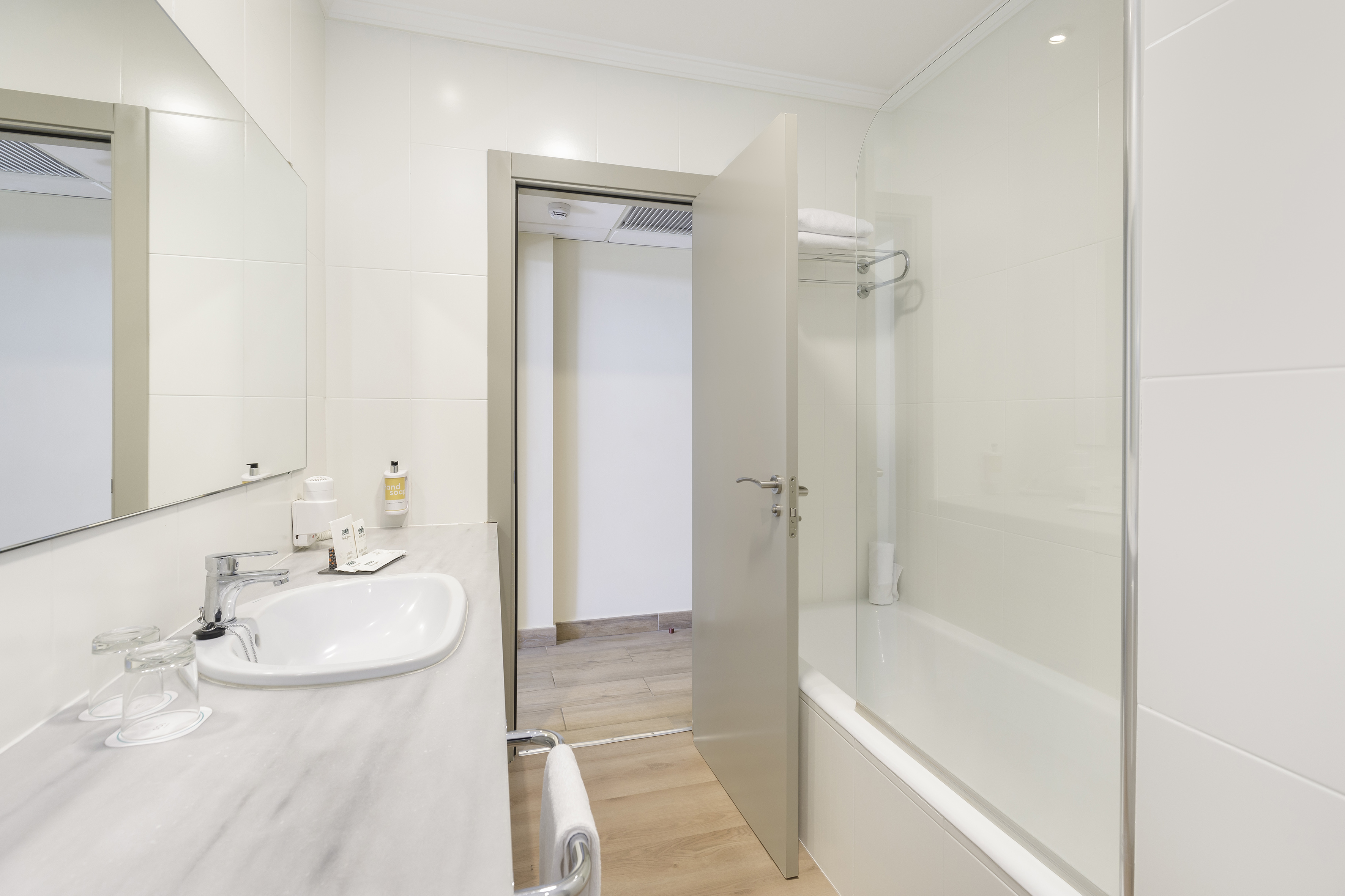 Clean white hotel bathroom with vanity, sink, mirror, and bathtub with shower.