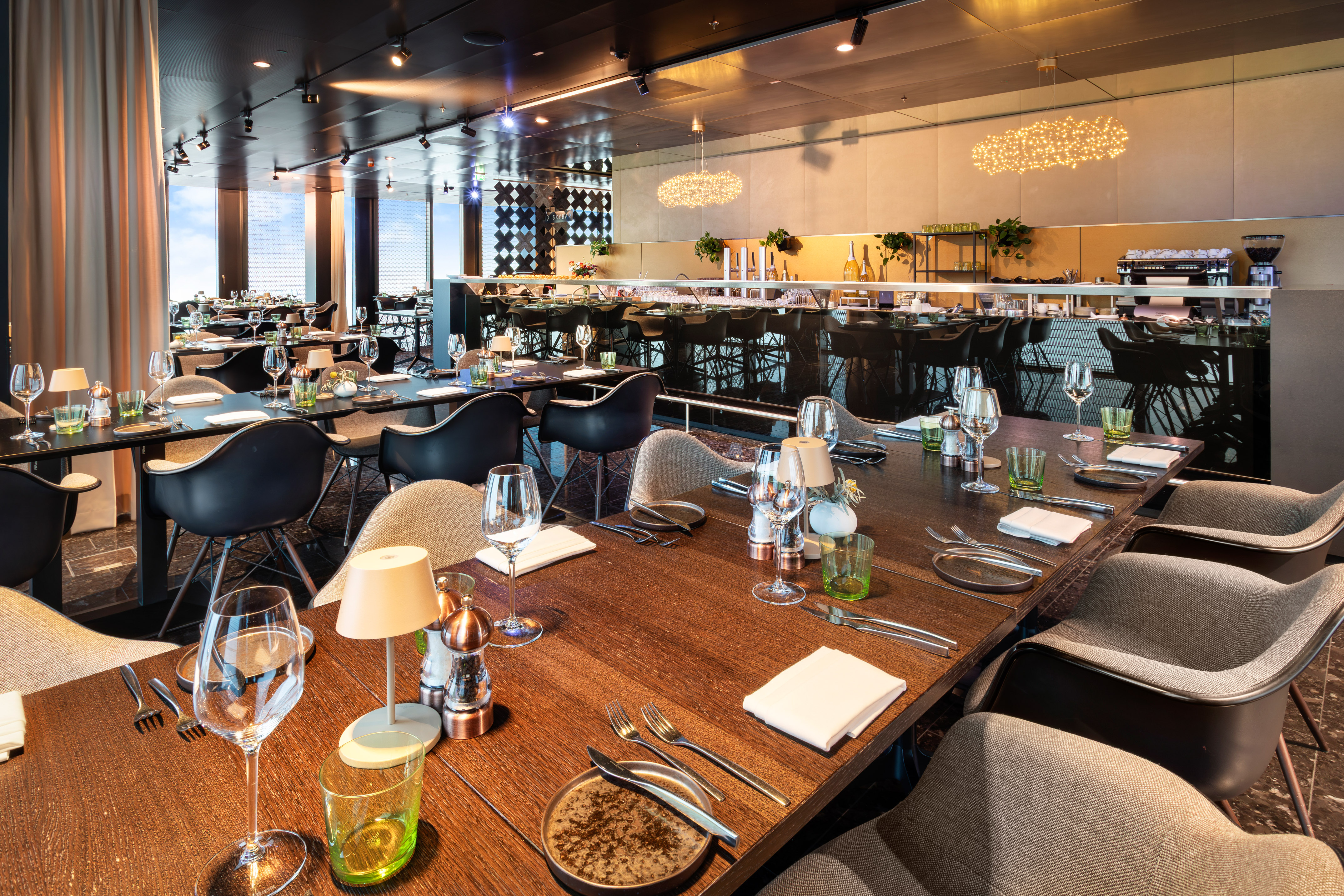 Modern restaurant dining room with set tables, comfortable chairs, and bar area.