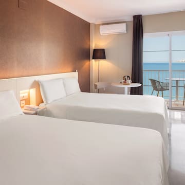 a room with two beds and a table and a balcony with a view of the ocean