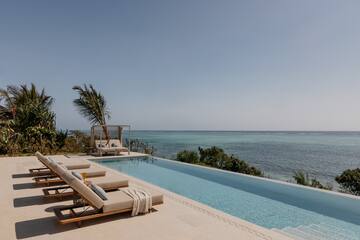 Oceanfront infinity pool with lounge chairs and tropical palm trees.