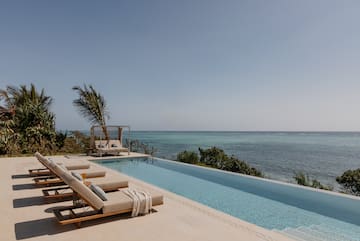 a pool with lounge chairs and a palm tree overlooking the ocean