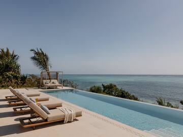 Oceanfront infinity pool with lounge chairs and tropical palm trees.