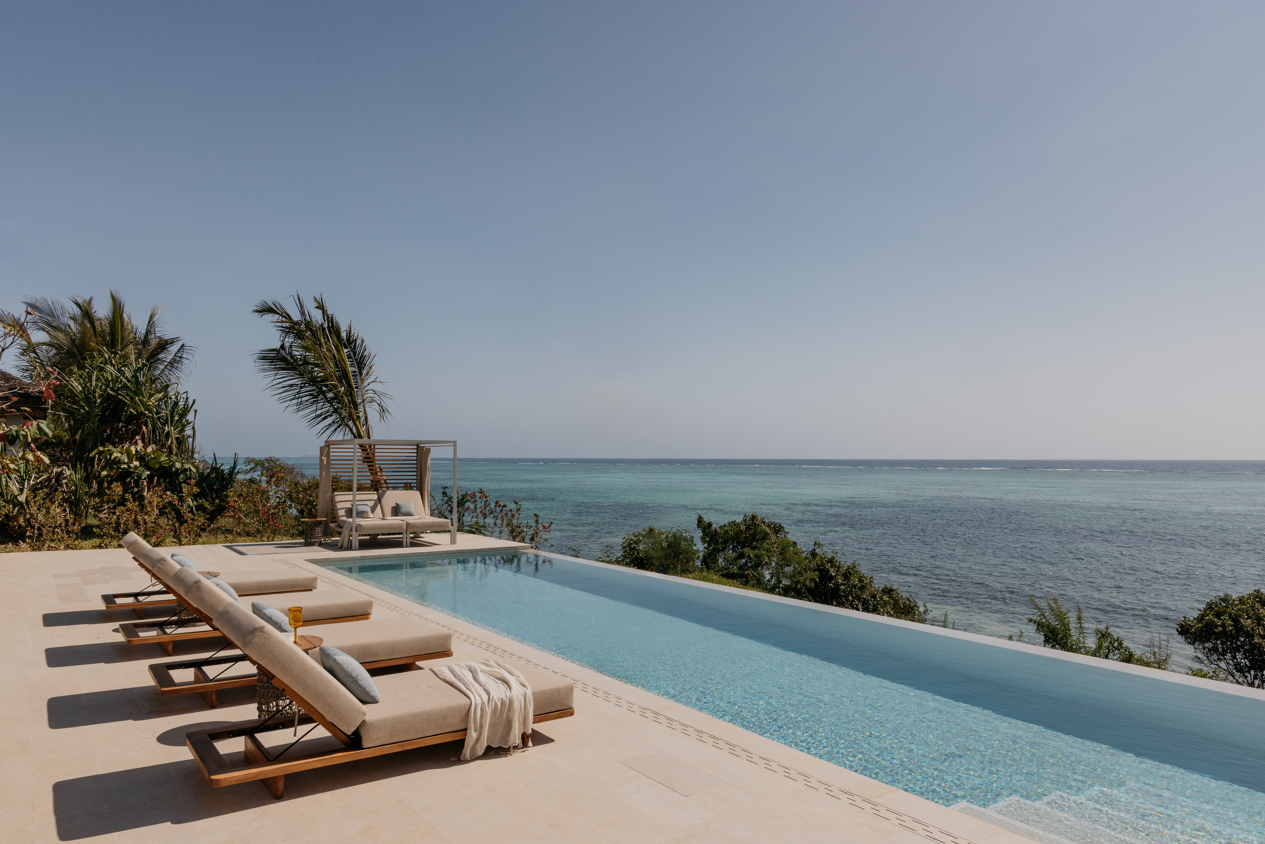 a pool with lounge chairs and a palm tree overlooking the ocean