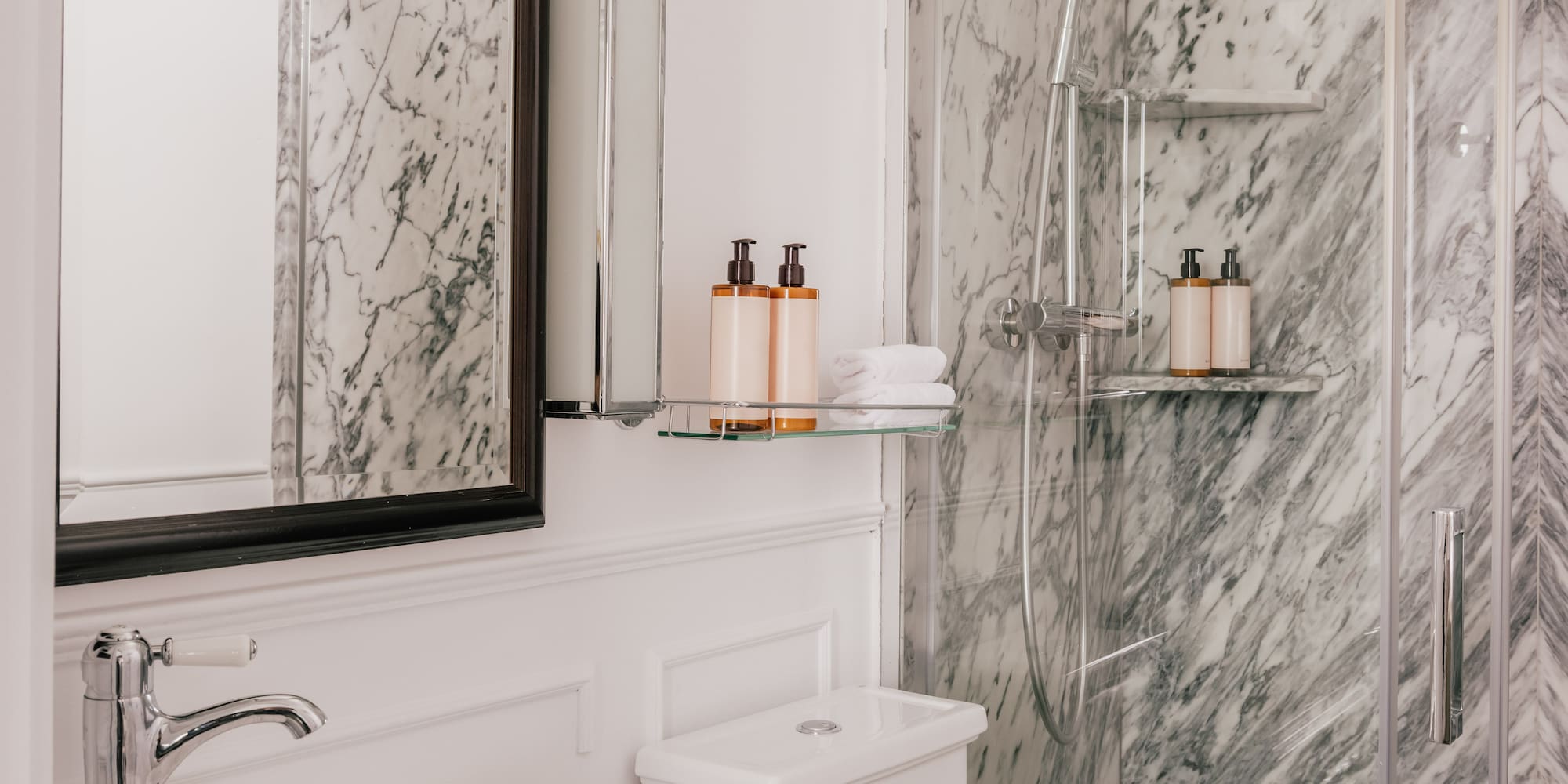 White marble bathroom with glass shower, modern vanity sink, and toilet.