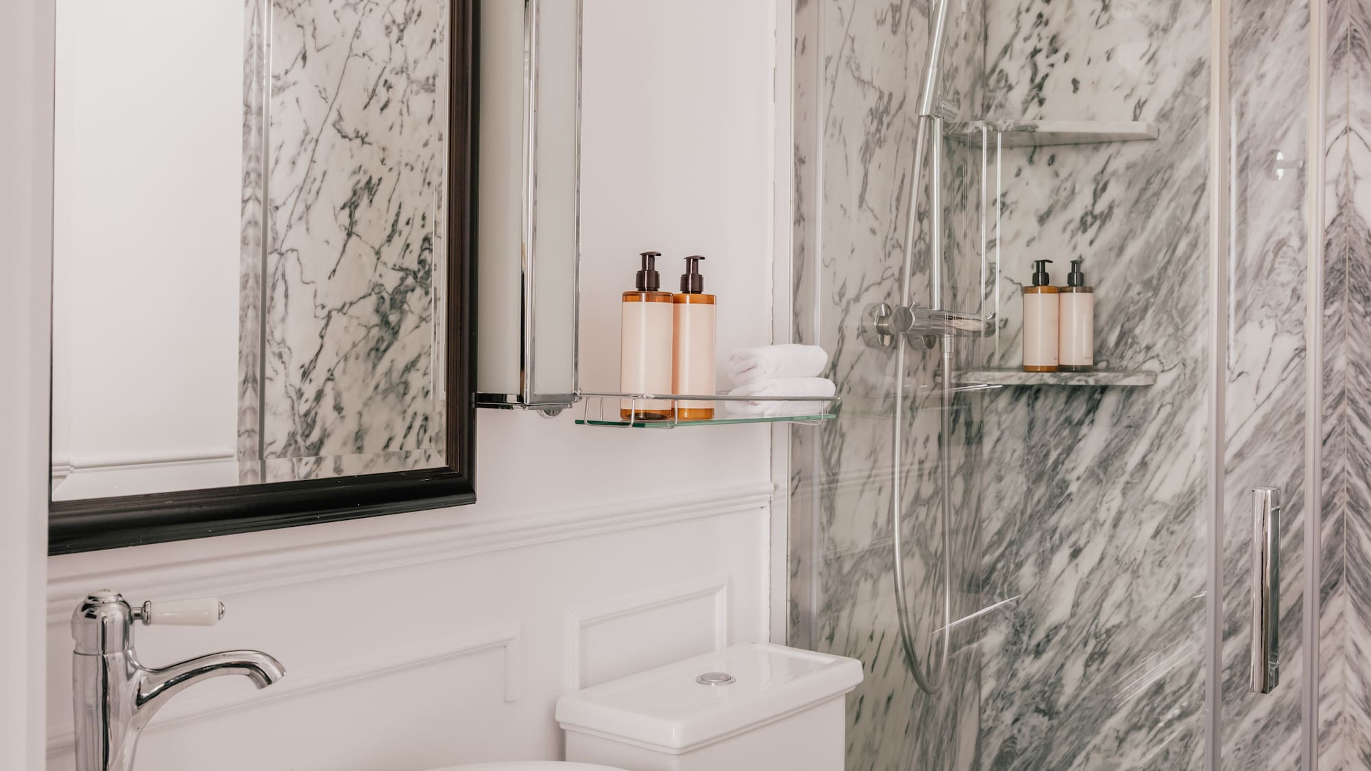 Sleek marble bathroom with glass shower, white vanity, vessel sink, and toilet.