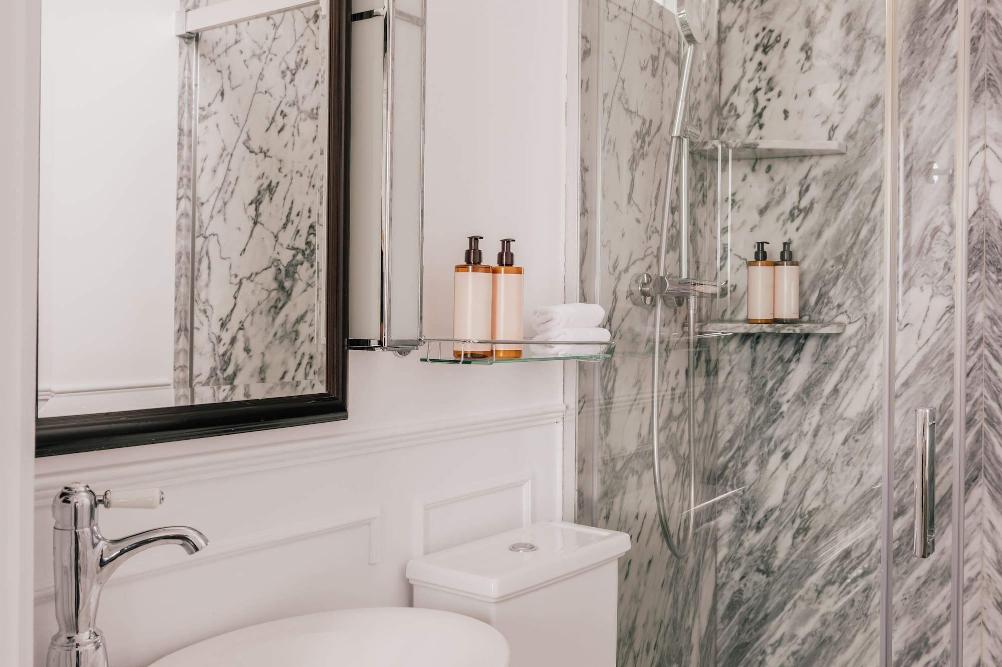 White marble bathroom with glass shower, modern vanity sink, and toilet.