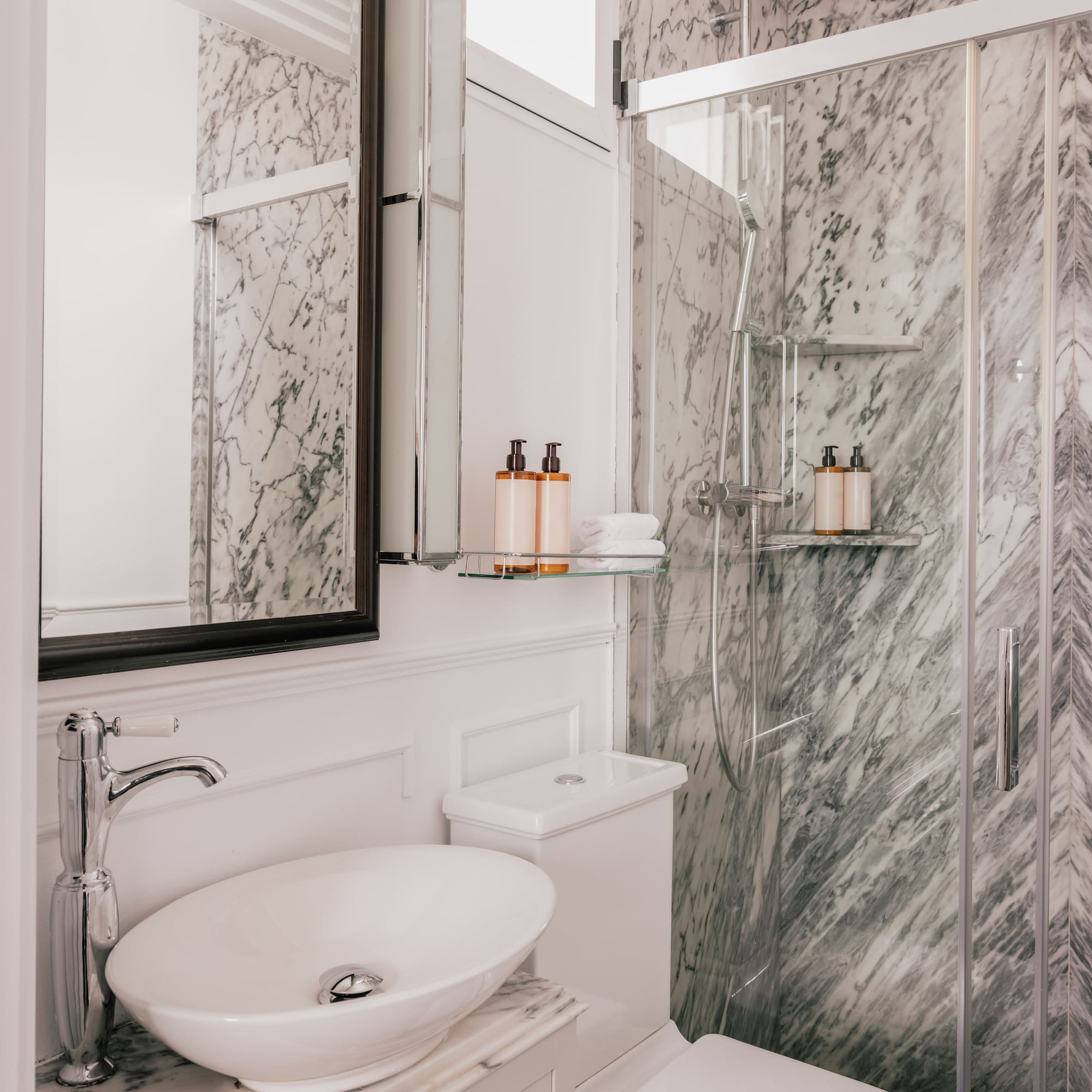 White marble bathroom with glass shower, modern vanity sink, and toilet.