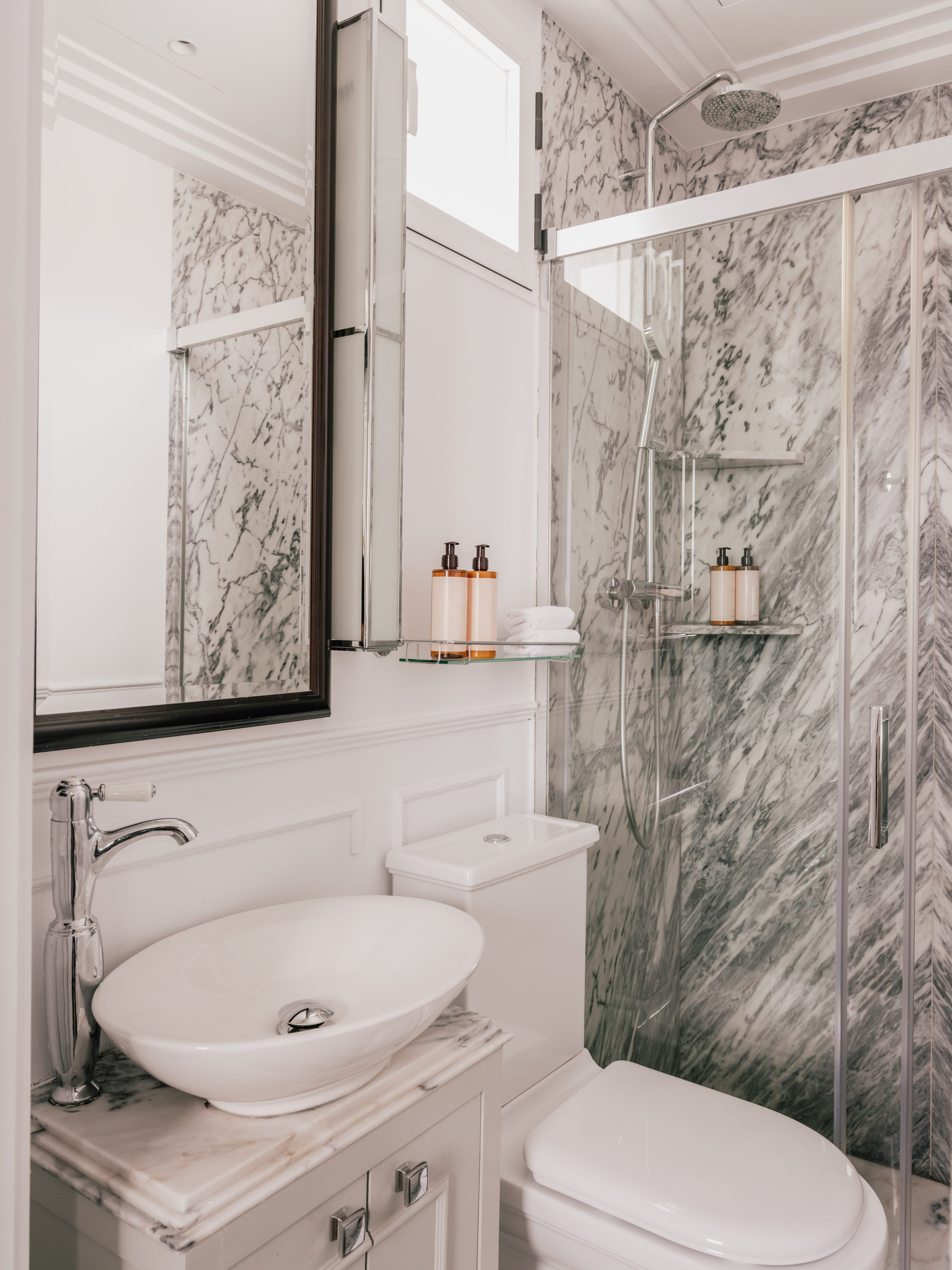 White marble bathroom with glass shower, modern vanity sink, and toilet.