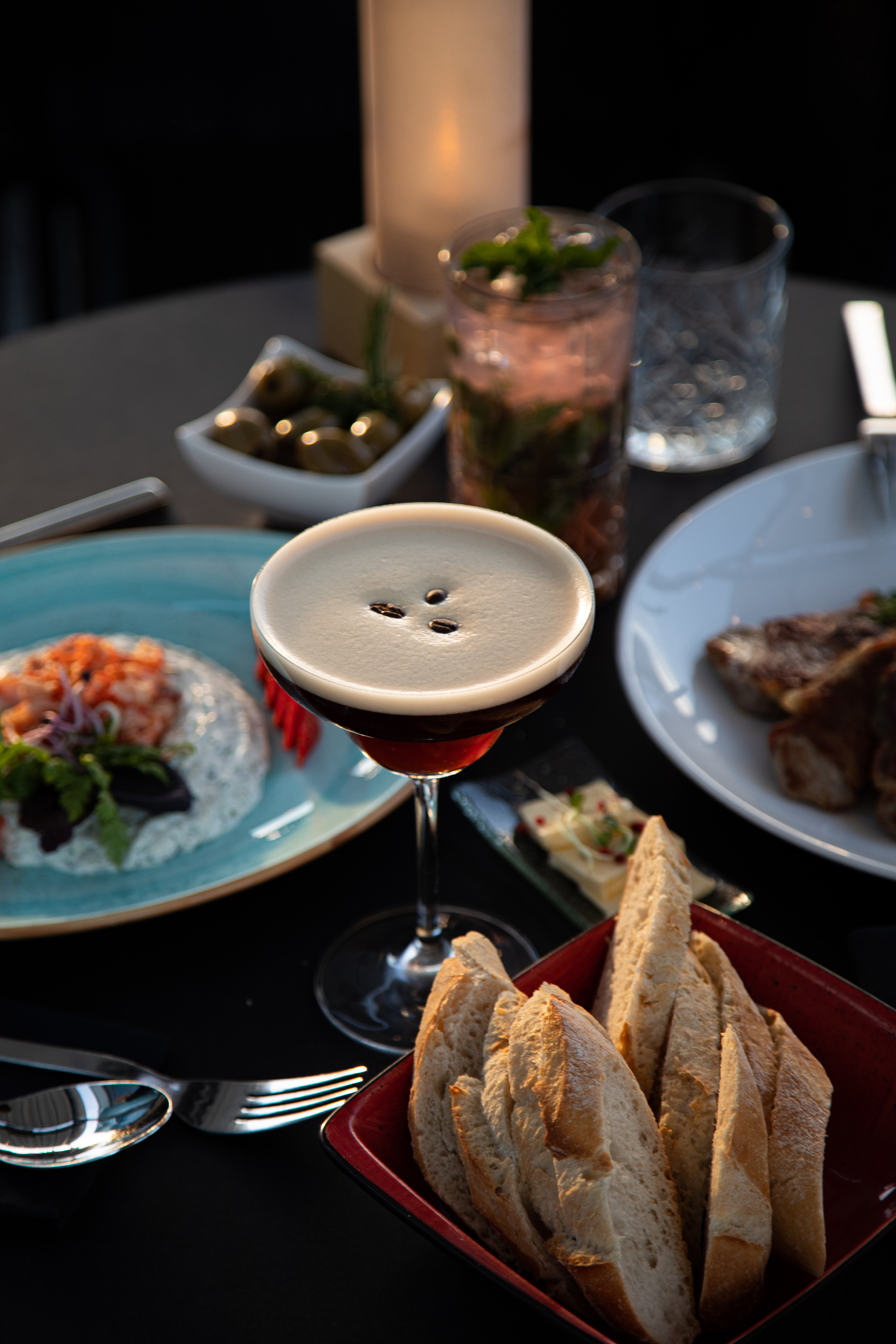 Espresso martini, seafood, steak, bread, and cocktails on a restaurant table.