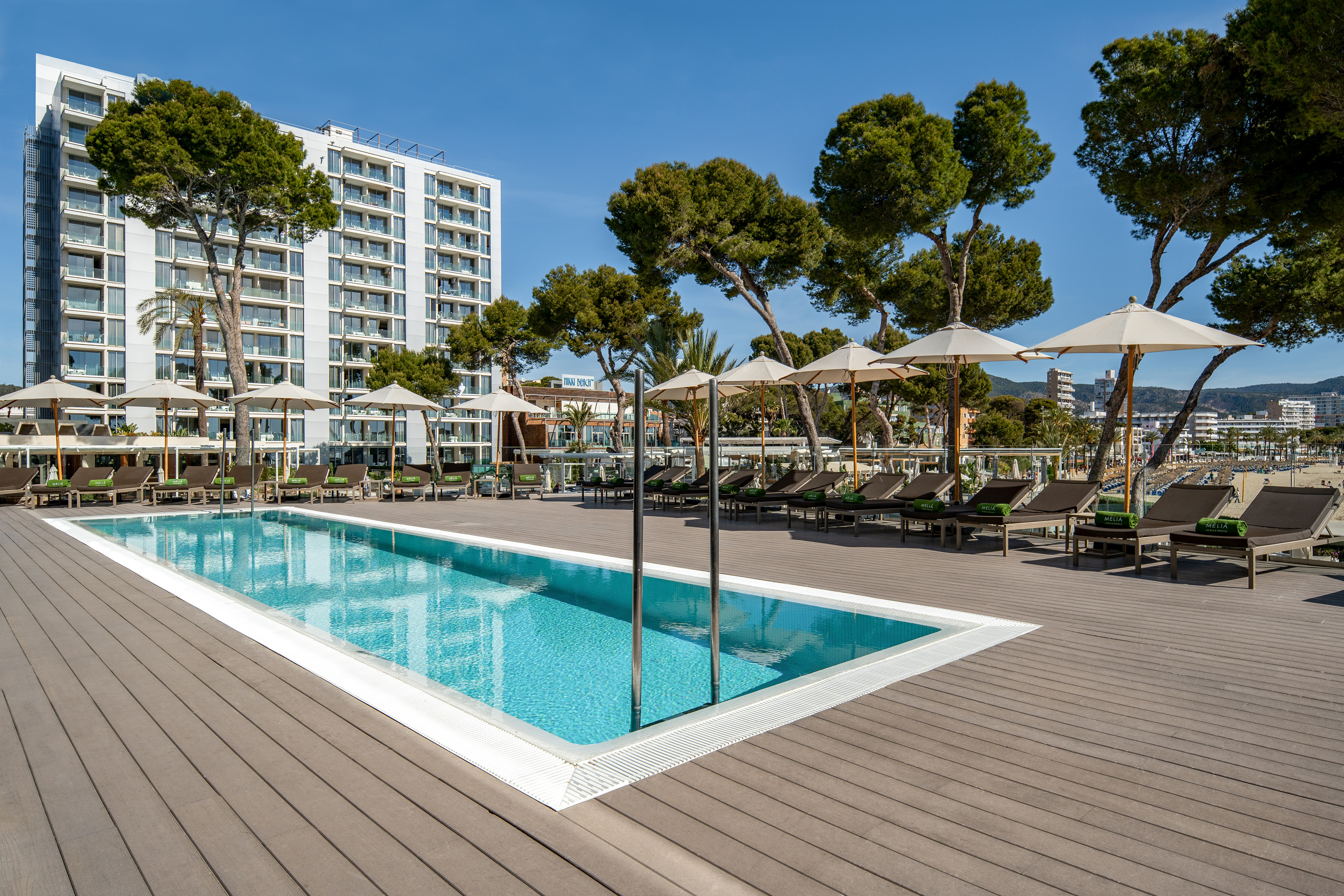 Modern resort pool deck with loungers, umbrellas, and hotel by beach.