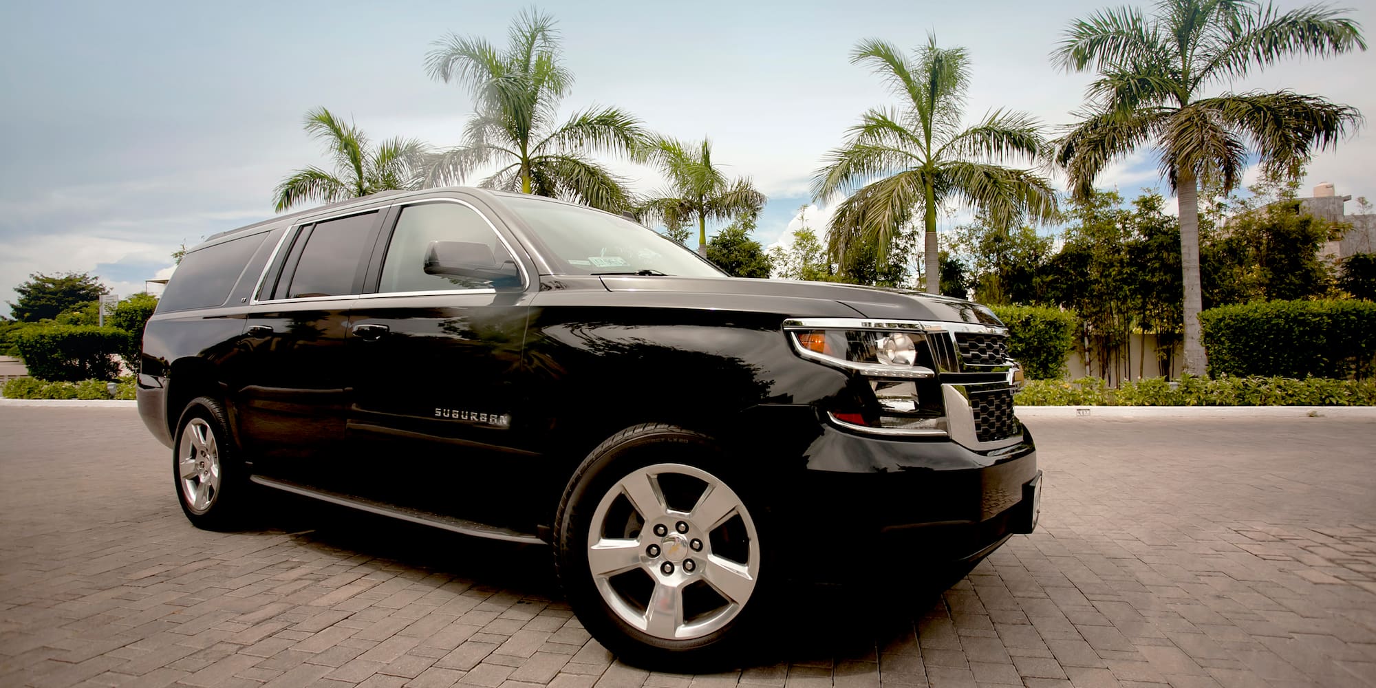 a black suv parked on brick road with palm trees in the background