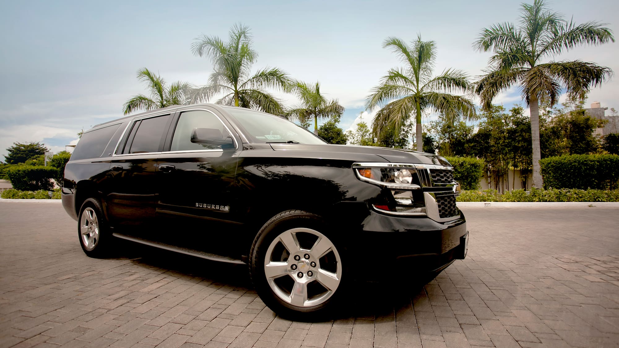 a black suv parked on brick road with palm trees in the background