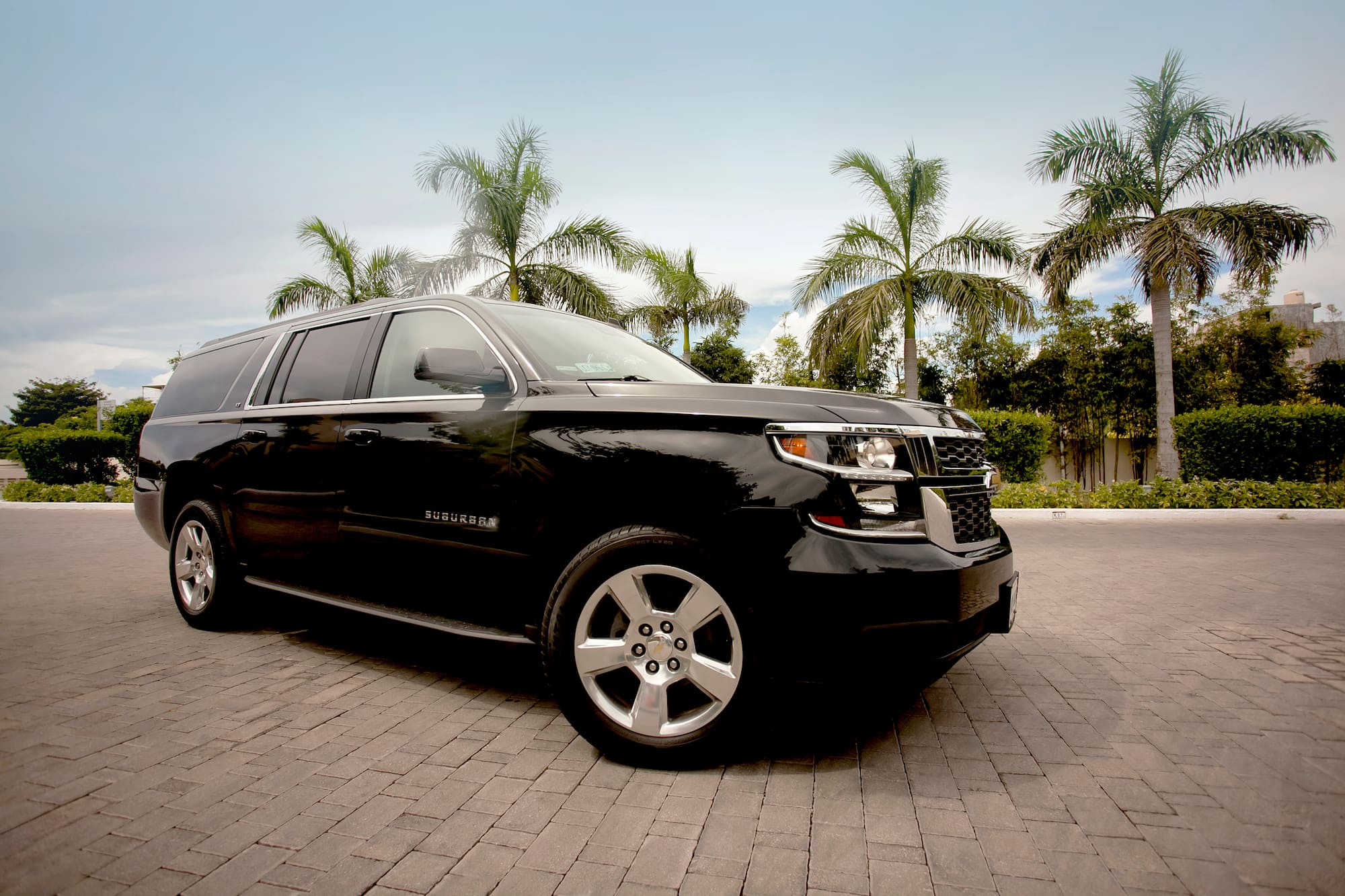 a black suv parked on brick road with palm trees in the background