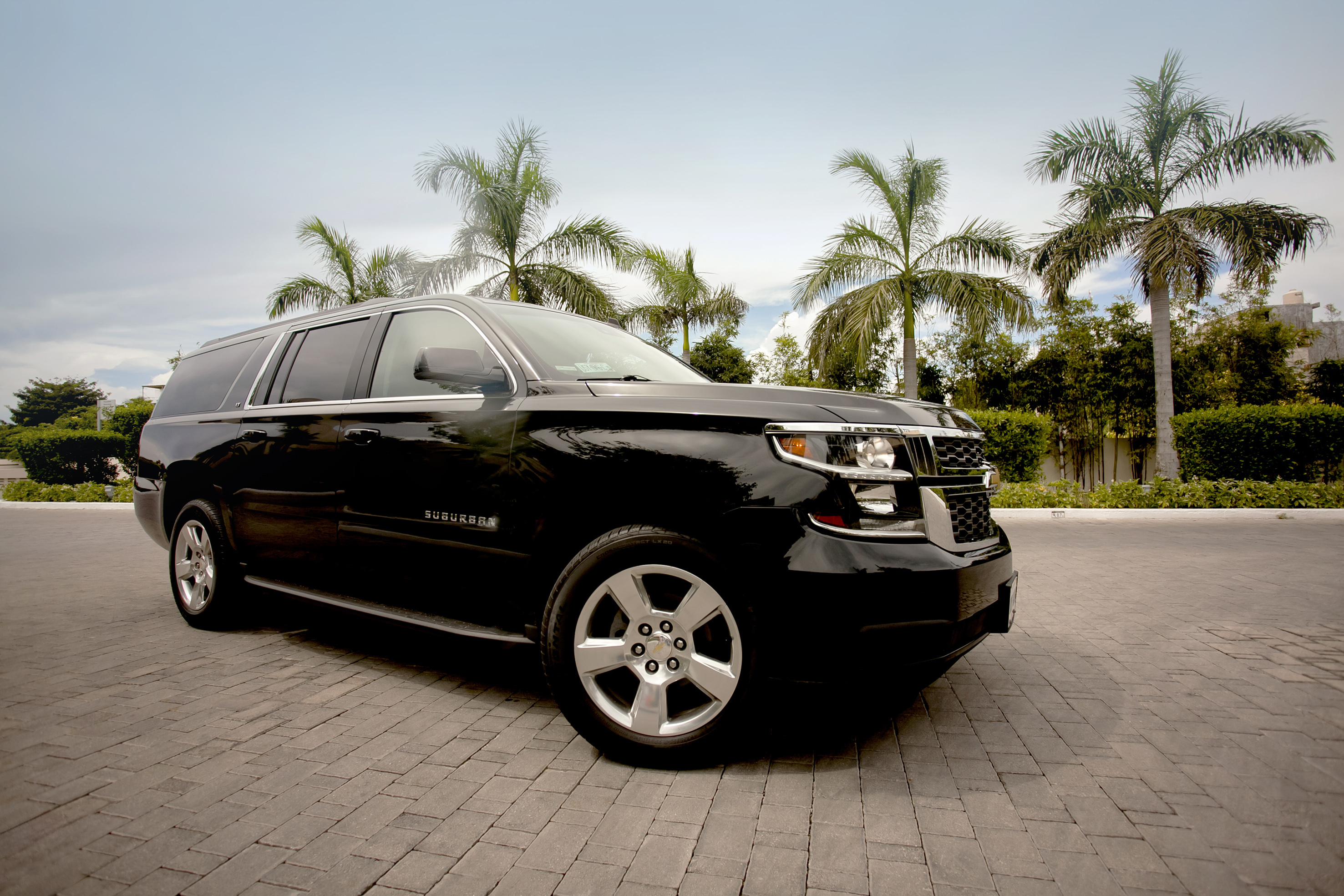 a black suv parked on brick road with palm trees in the background