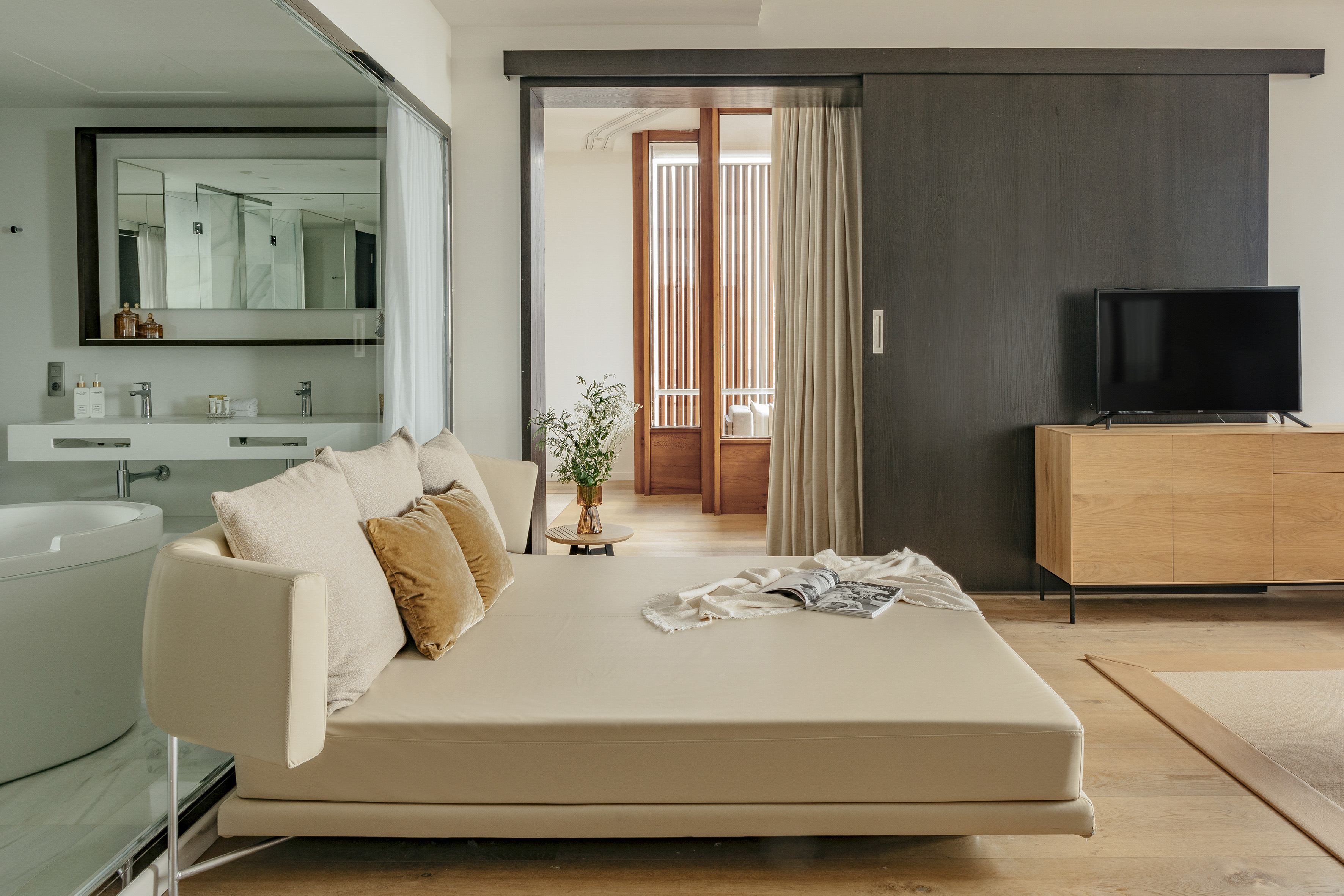 Luxury hotel room with sleek daybed, wood floor, and open bathroom.