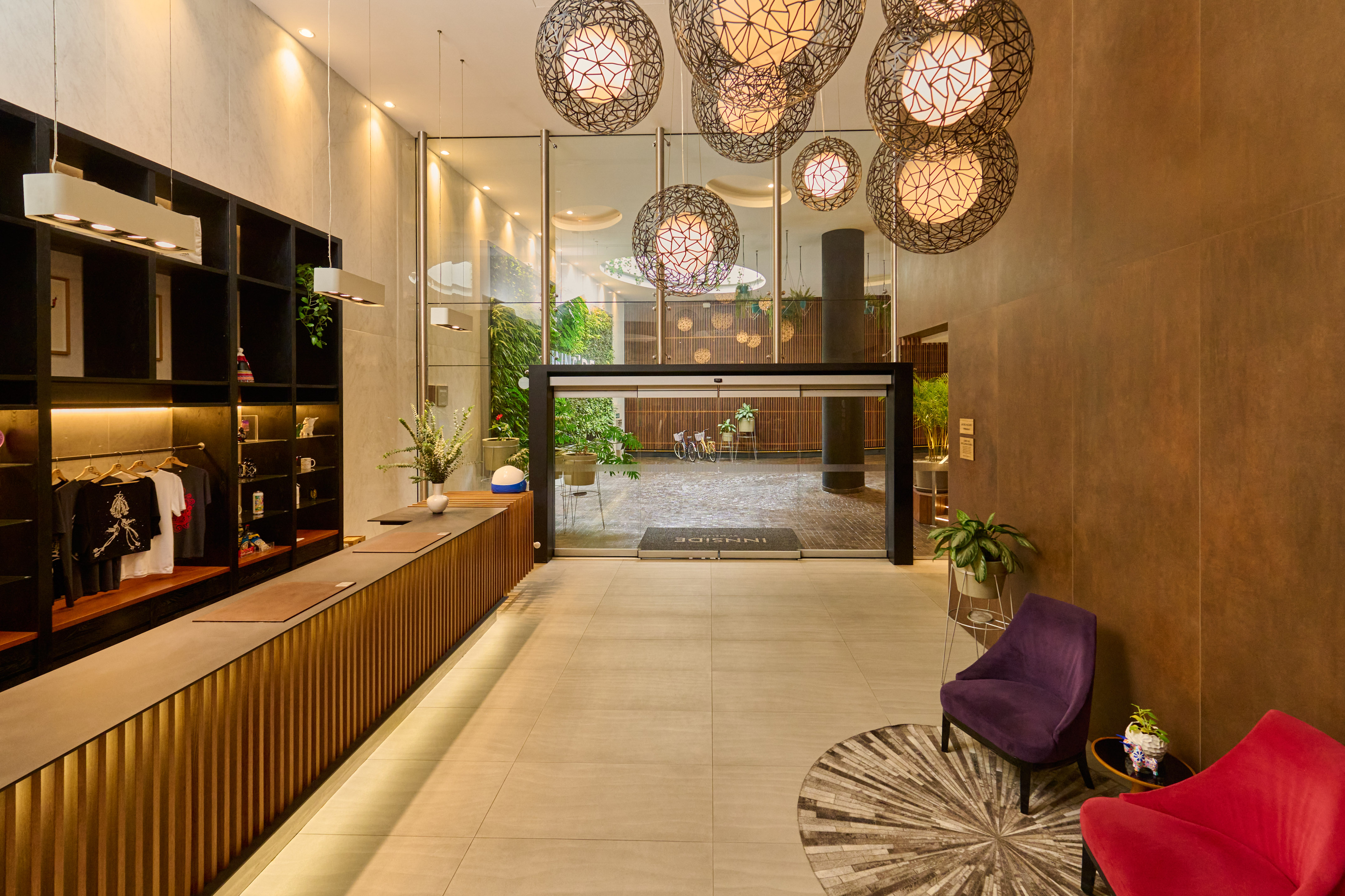 Hotel lobby with sleek reception, geometric pendant lights, and green courtyard.