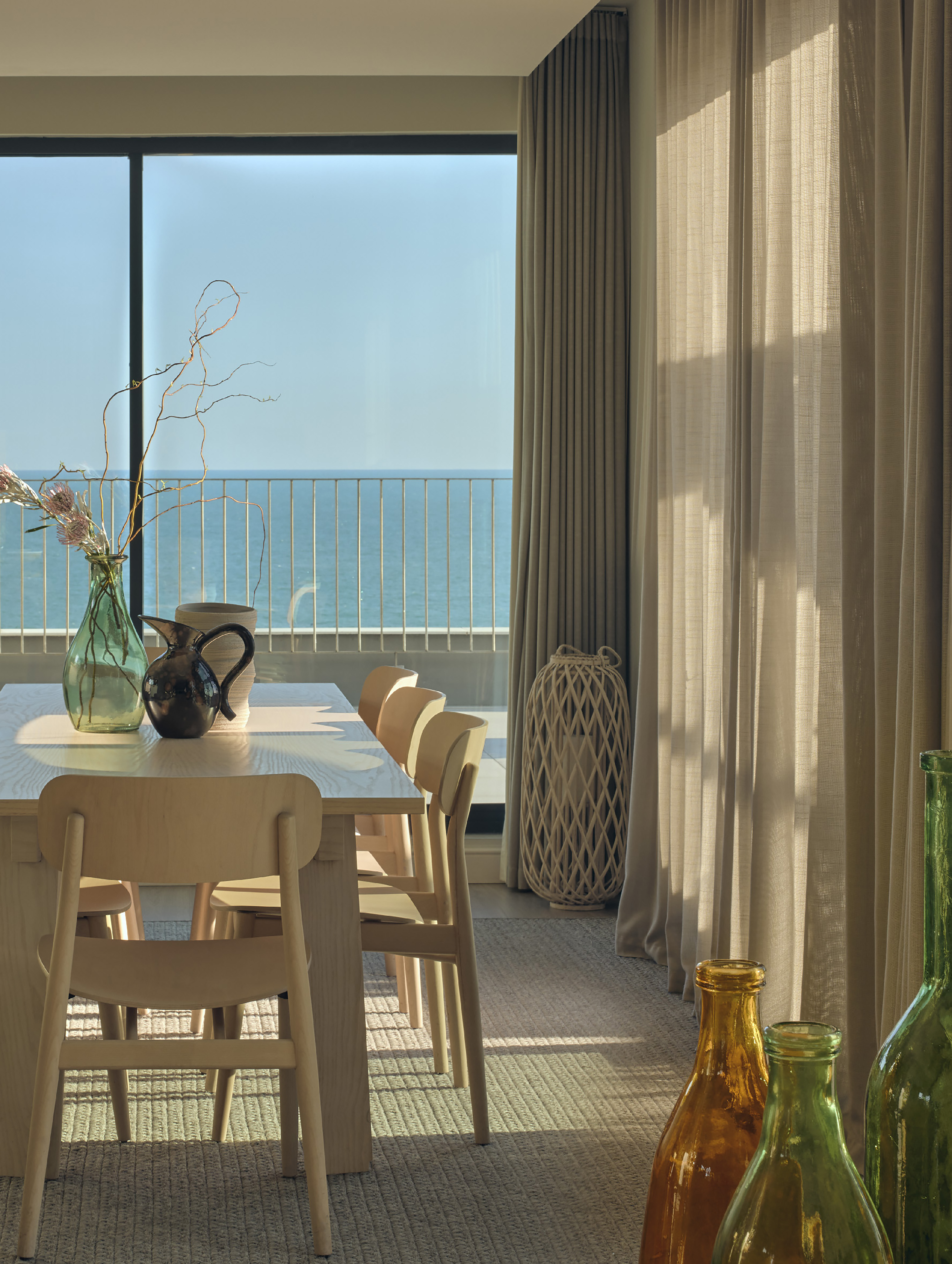 Modern dining room, panoramic ocean view, wood table, and sunlit sheer curtains.