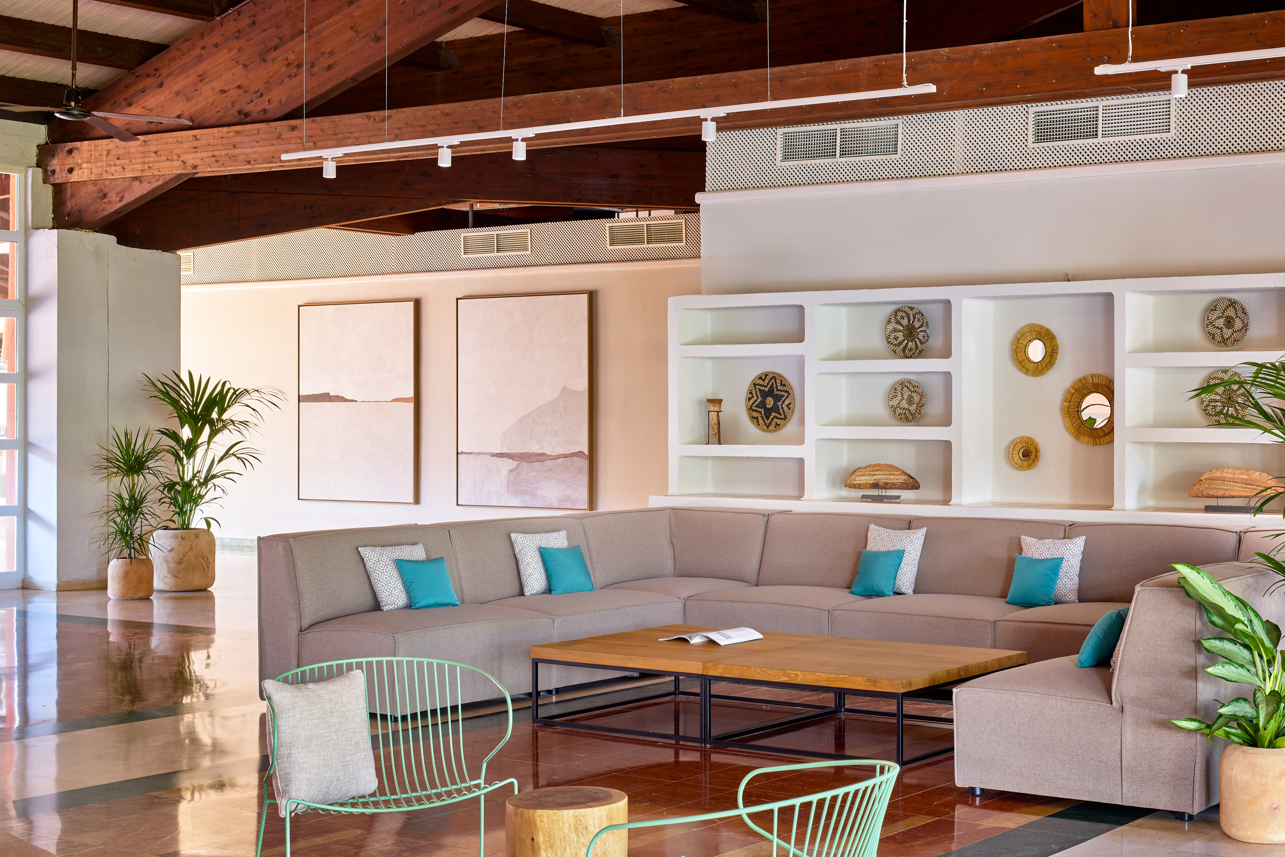 Spacious hotel lounge with sectional sofa, wooden beams, plants, and wall decor.