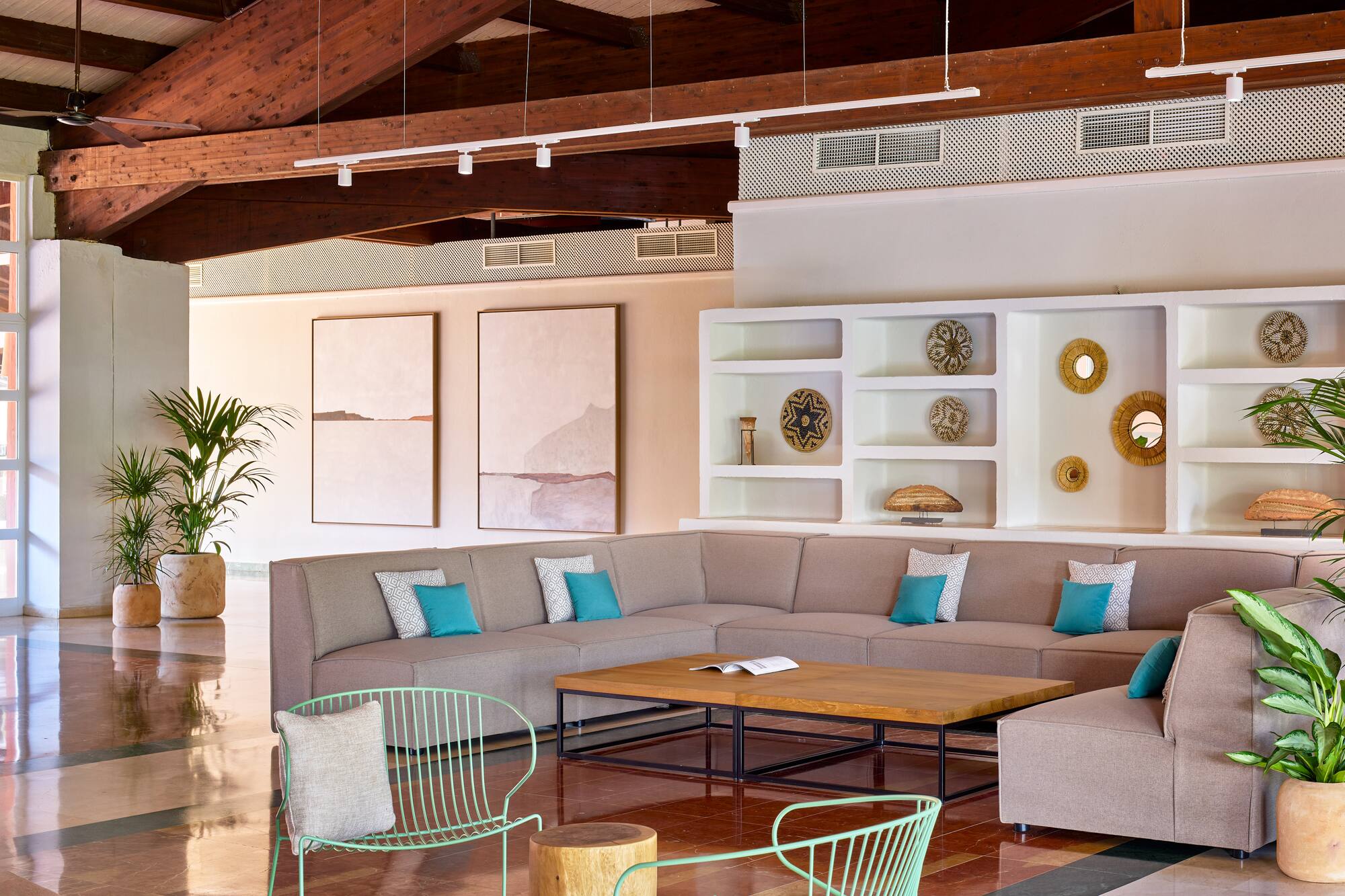 Spacious hotel lounge with sectional sofa, wooden beams, plants, and wall decor.