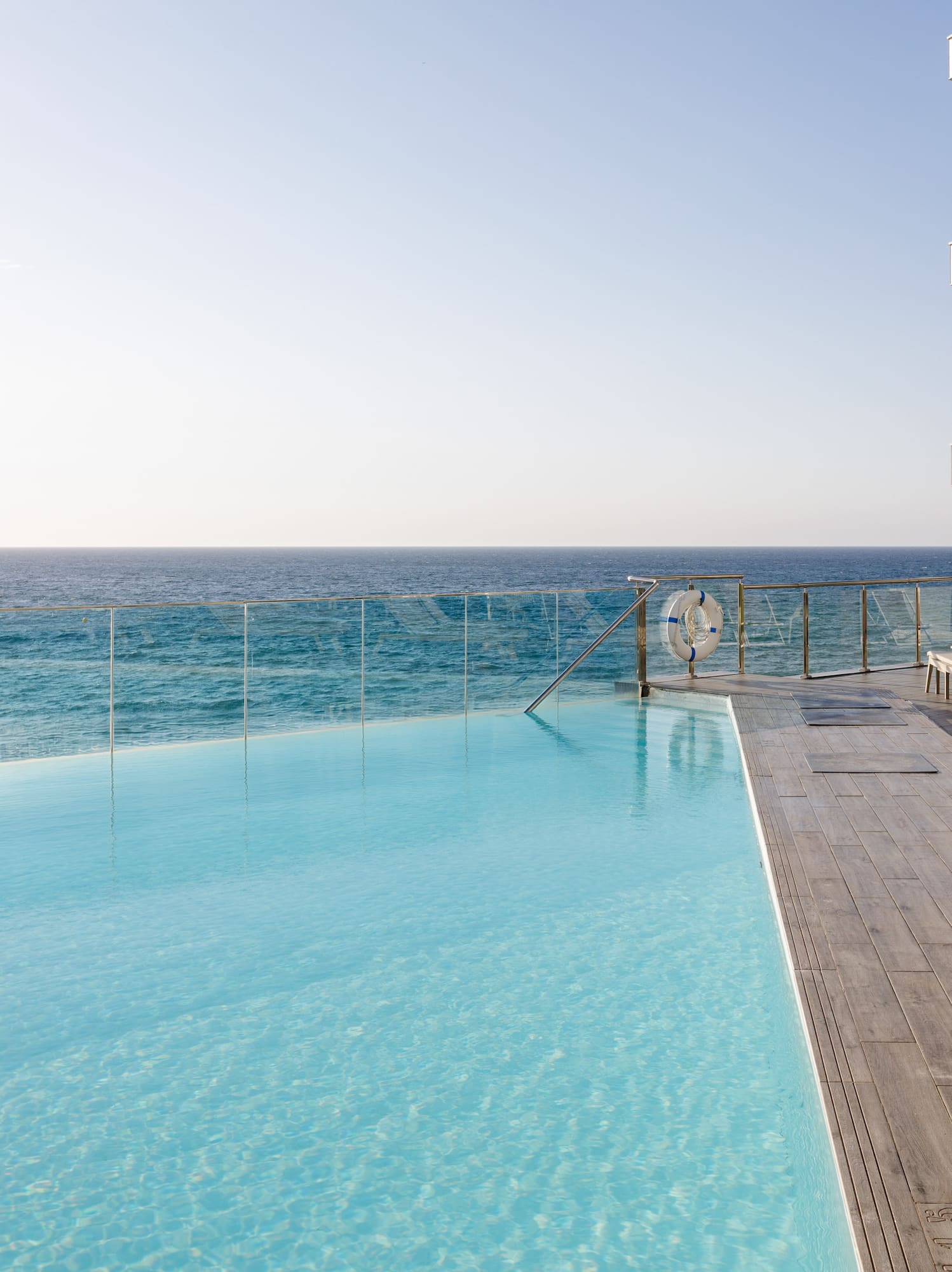 Piscina infinita con vista al océano, hotel moderno con terraza y tumbonas.