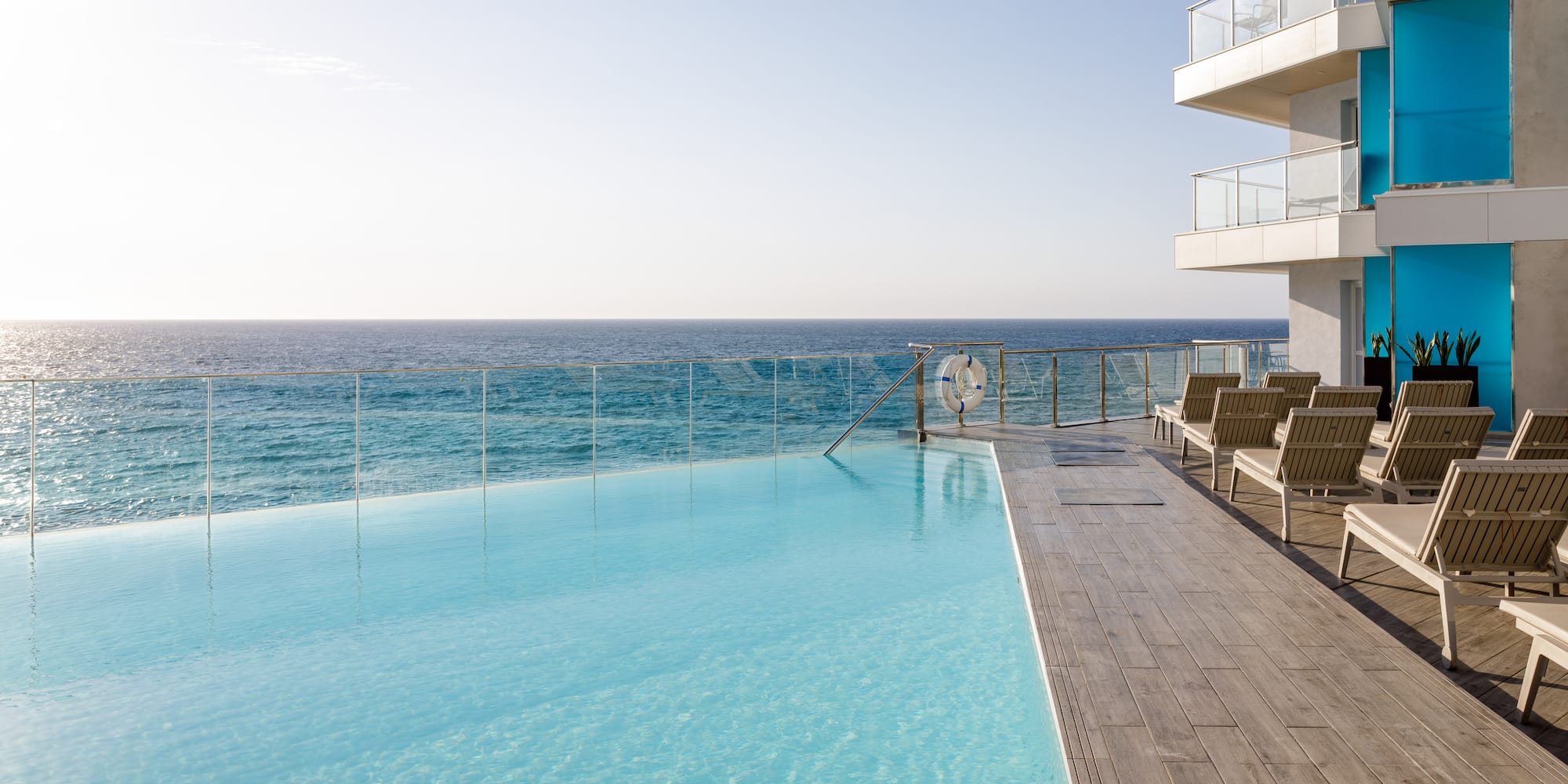 Piscina infinita de hotel frente al mar con tumbonas en terraza moderna.