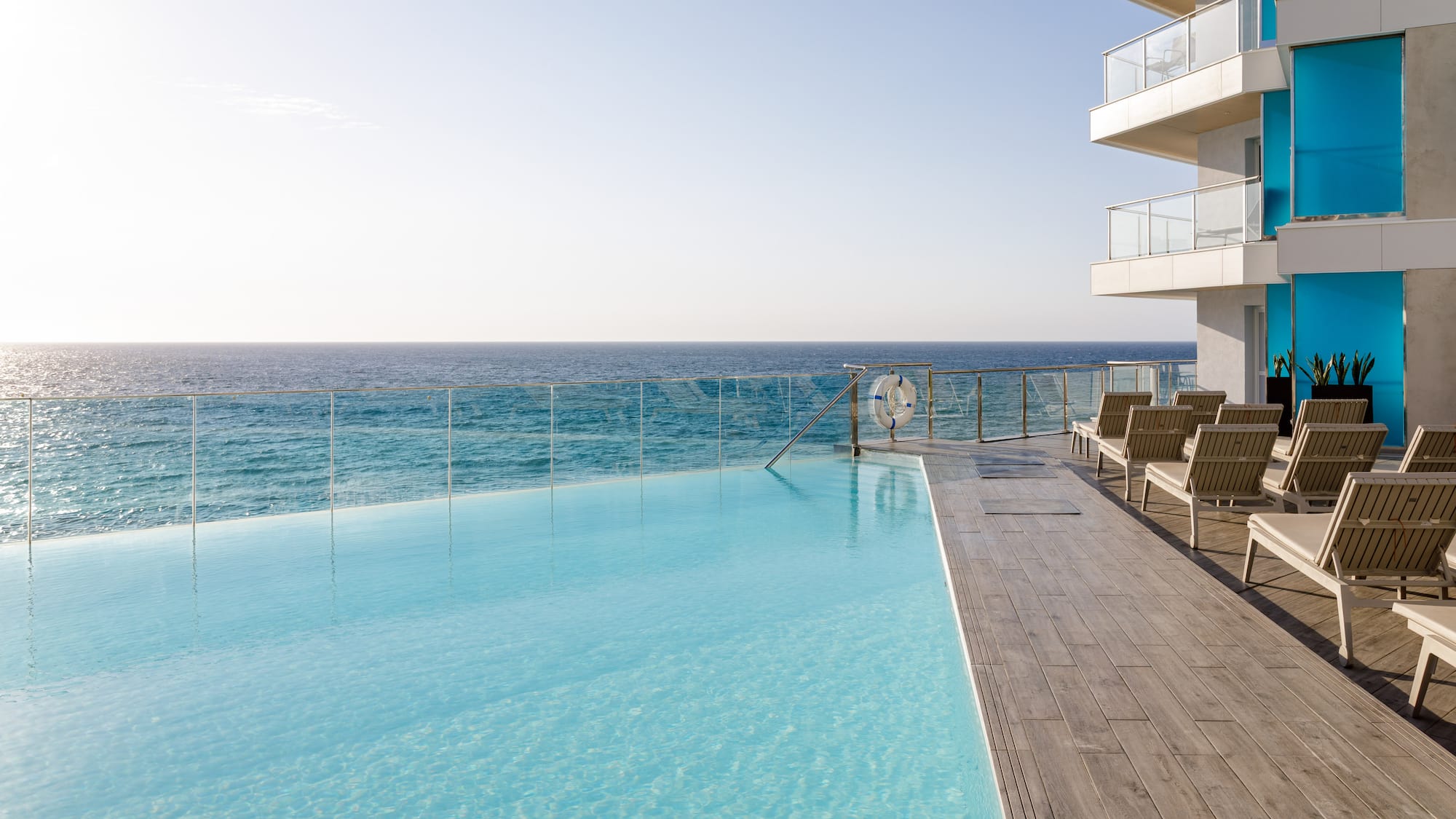 Piscina infinita de hotel frente al mar con tumbonas en terraza moderna.