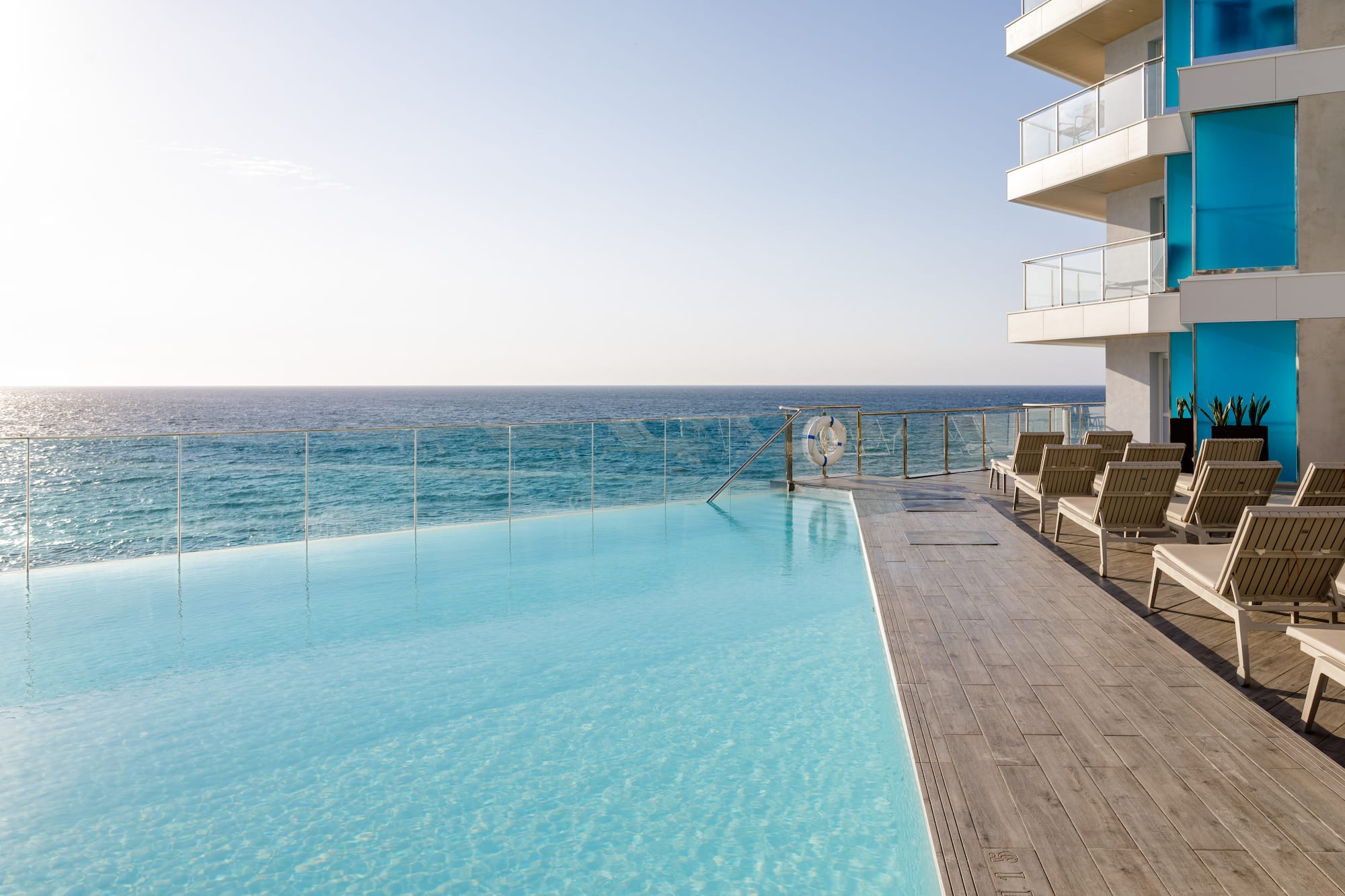 Piscina infinita de hotel con vista al mar y edificio azul.