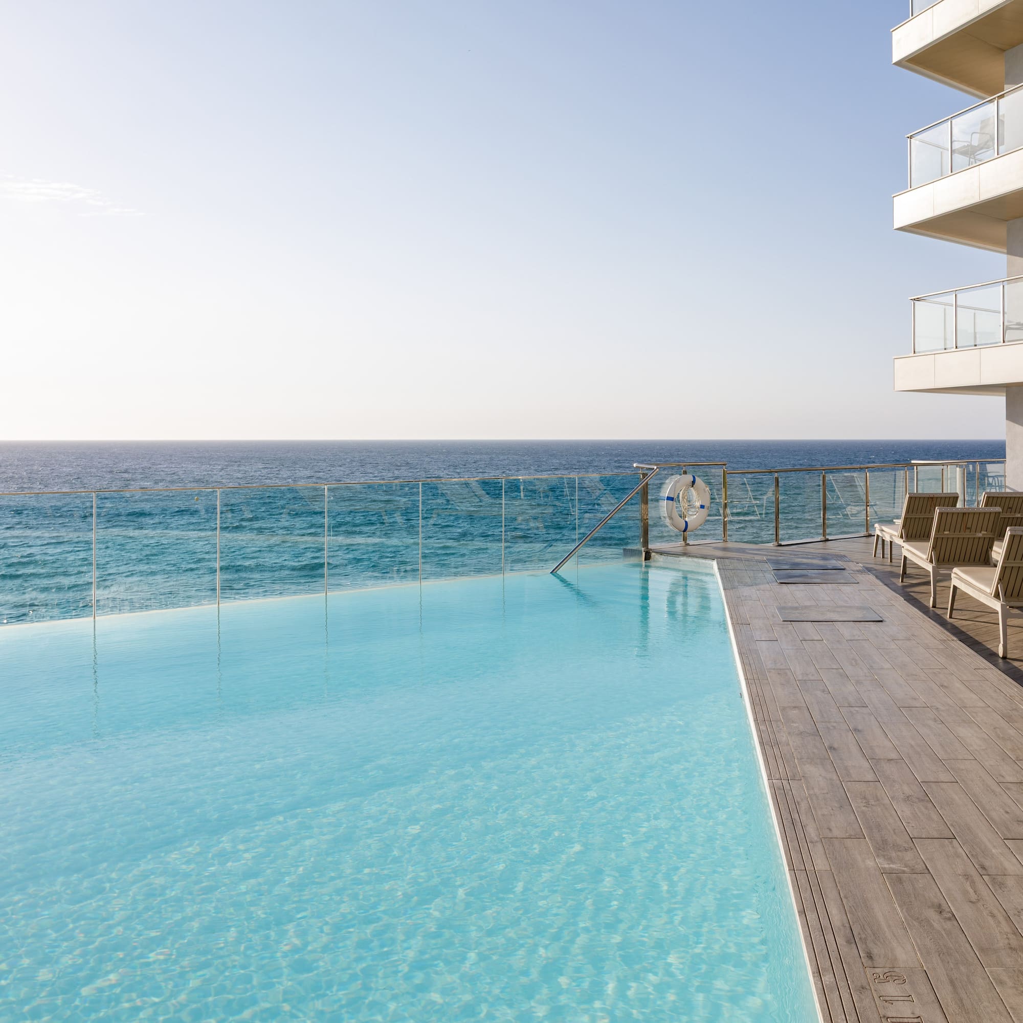 Piscina infinita azul en hotel moderno con vistas al mar y tumbonas.
