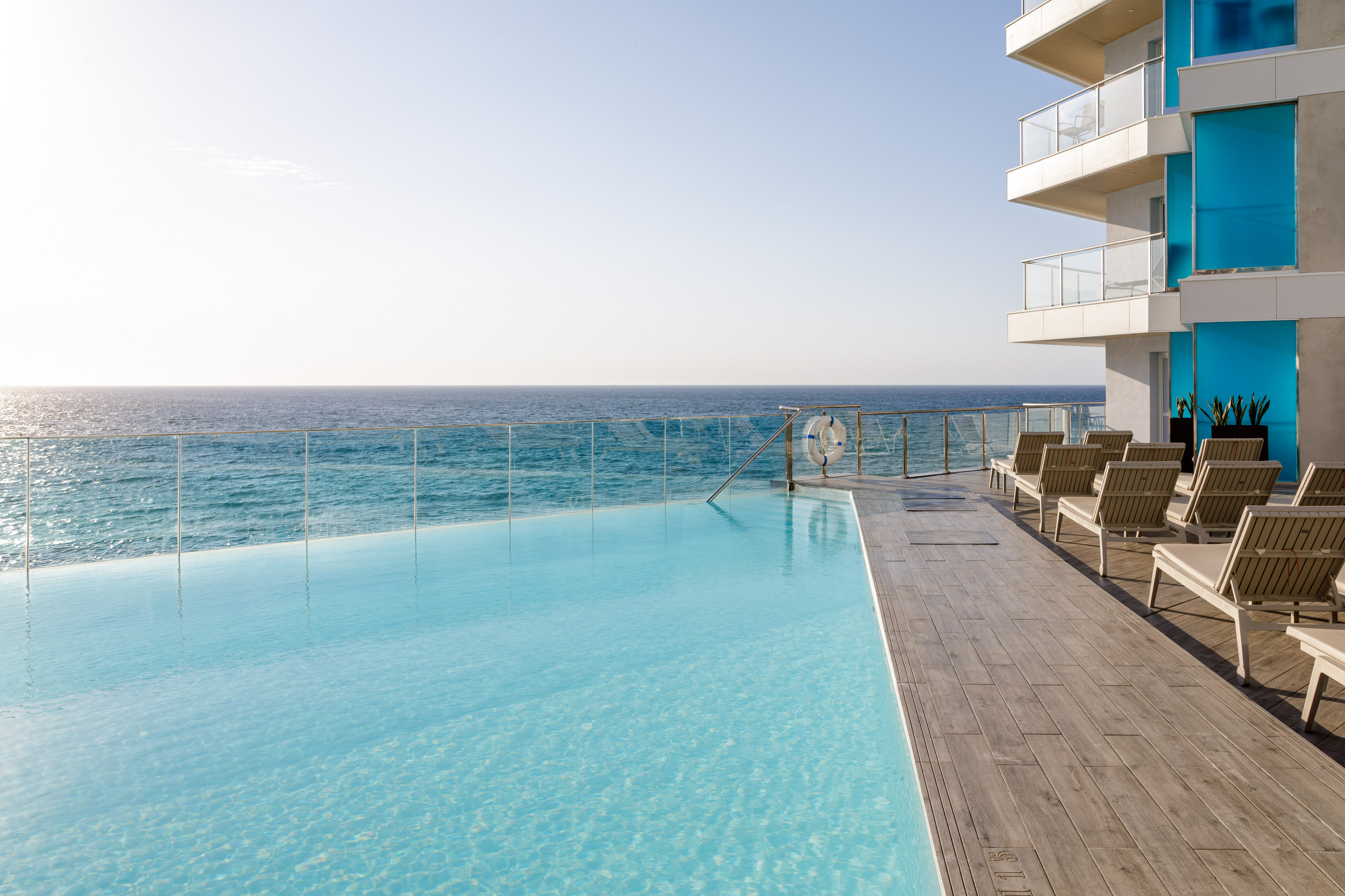 Piscina infinita de hotel frente al mar con tumbonas en terraza moderna.