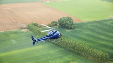a blue helicopter flying over a green field