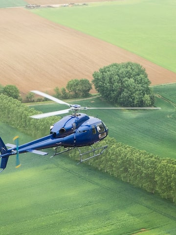 a blue helicopter flying over a green field