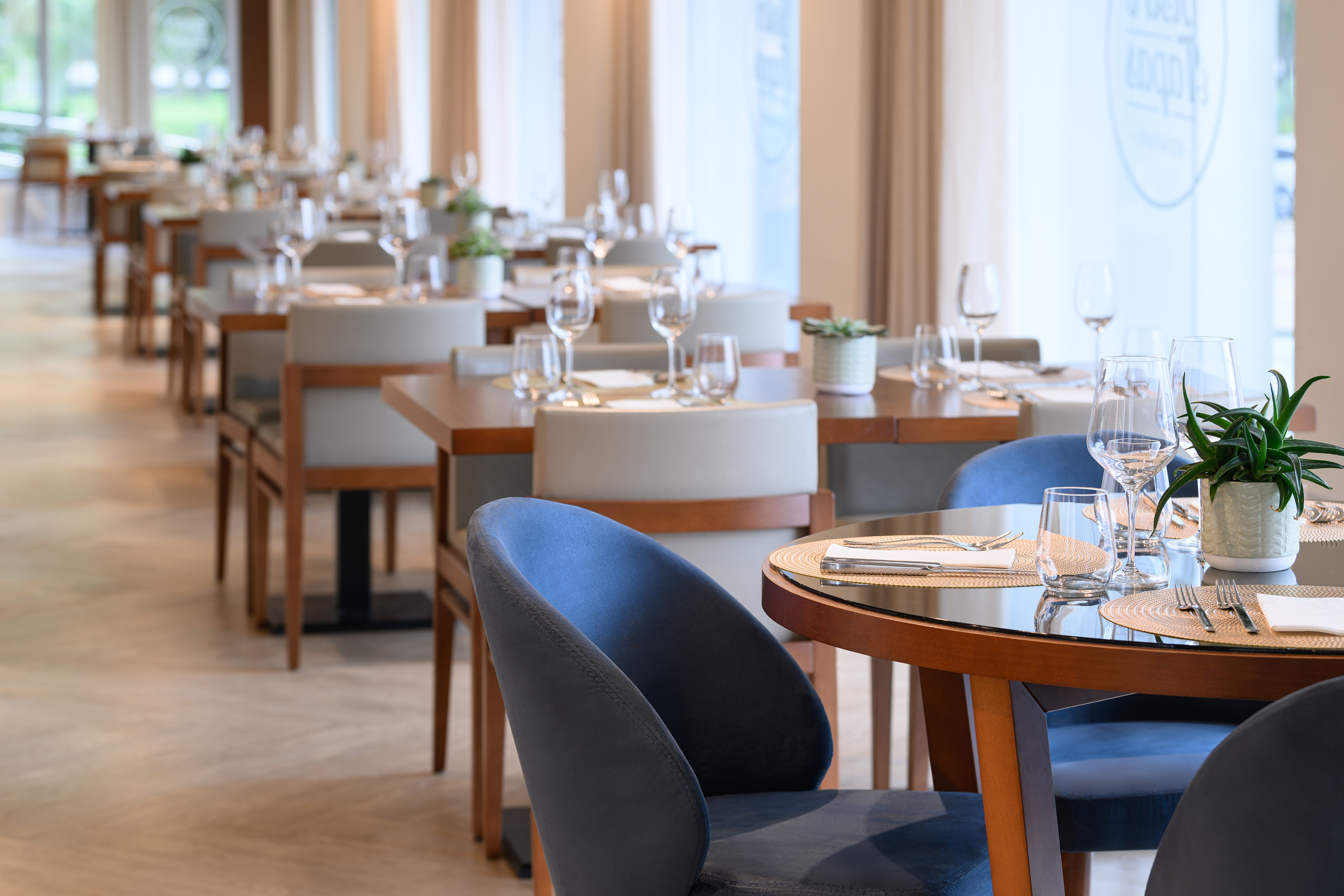 Bright modern restaurant dining room with neatly set tables and blue chairs.