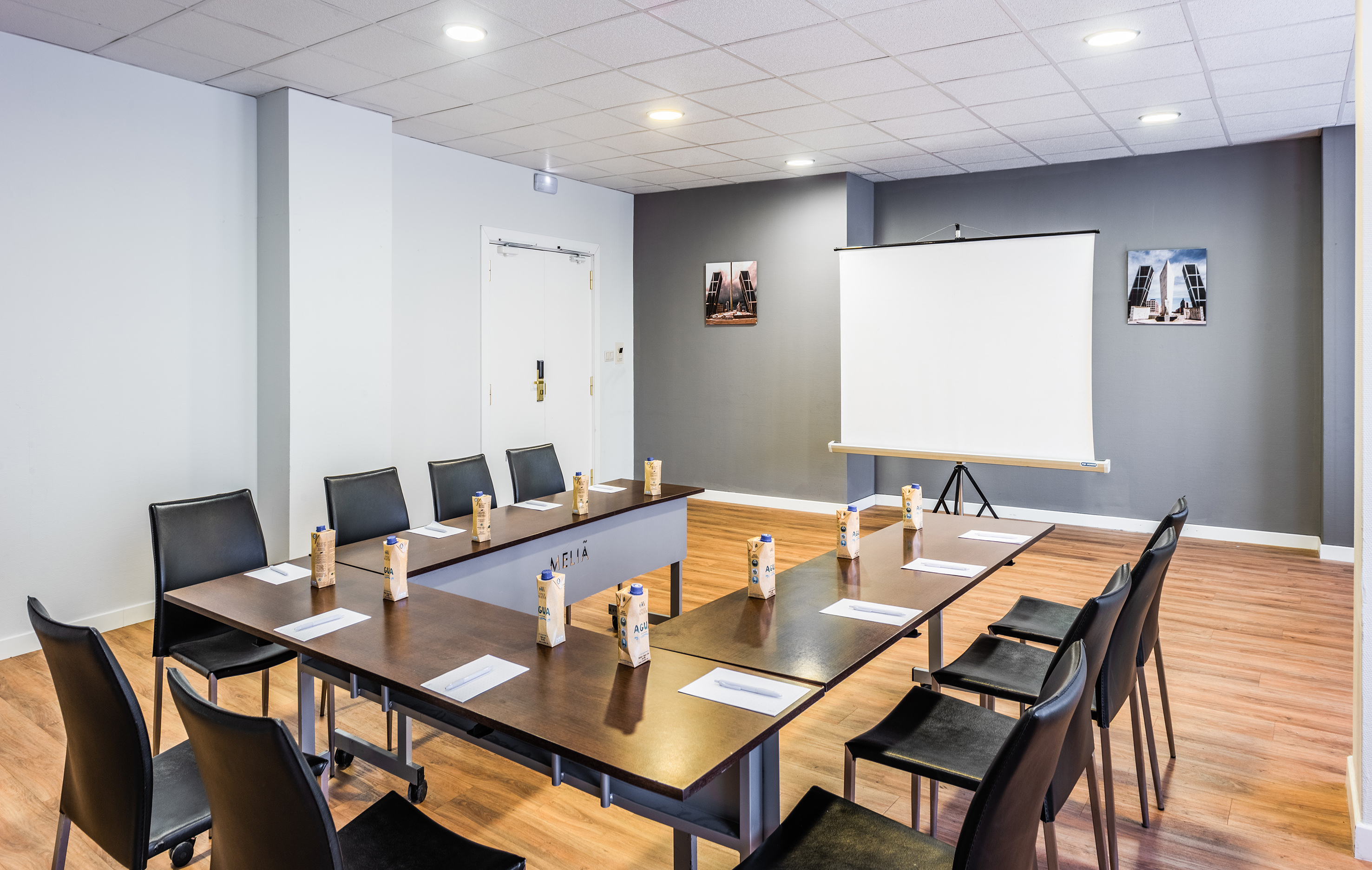 Modern meeting room with U-shaped table, chairs, projector screen, and refreshments.